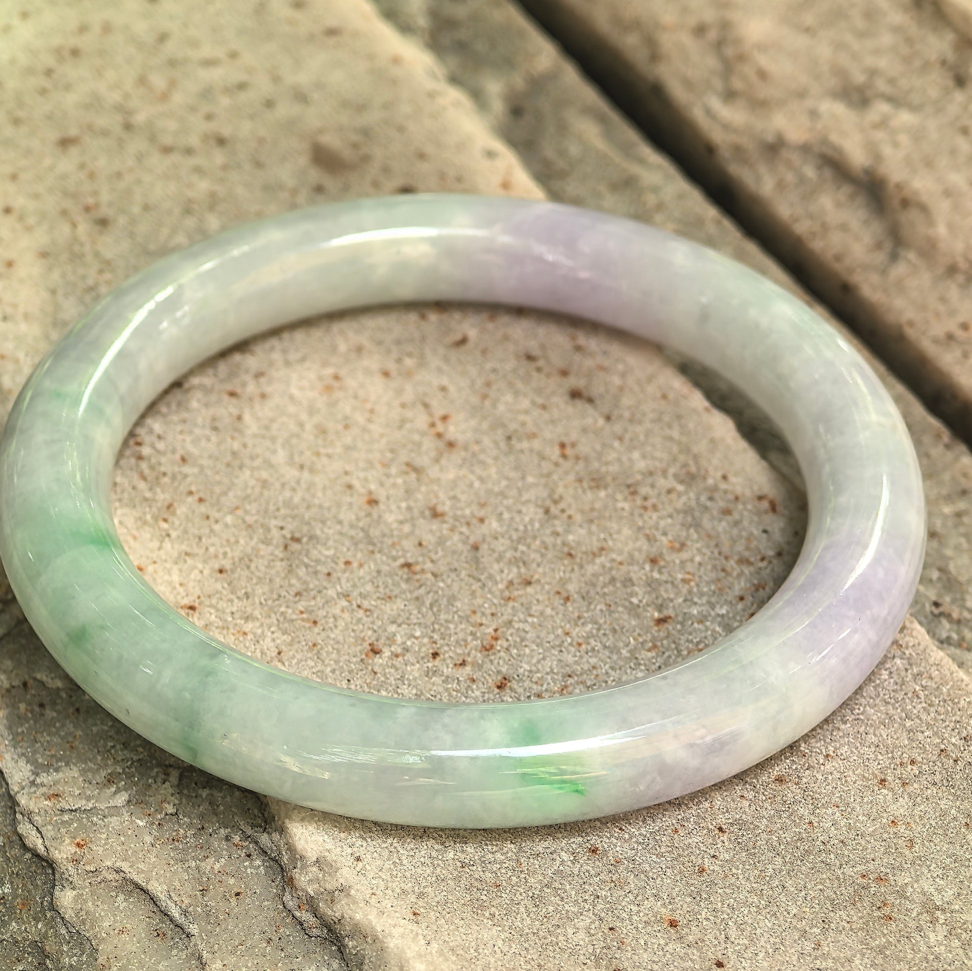 Natural Grade-A glutinous lavender-green jadeite round bangle displayed on stone, showing its polished surface and mixed colors.