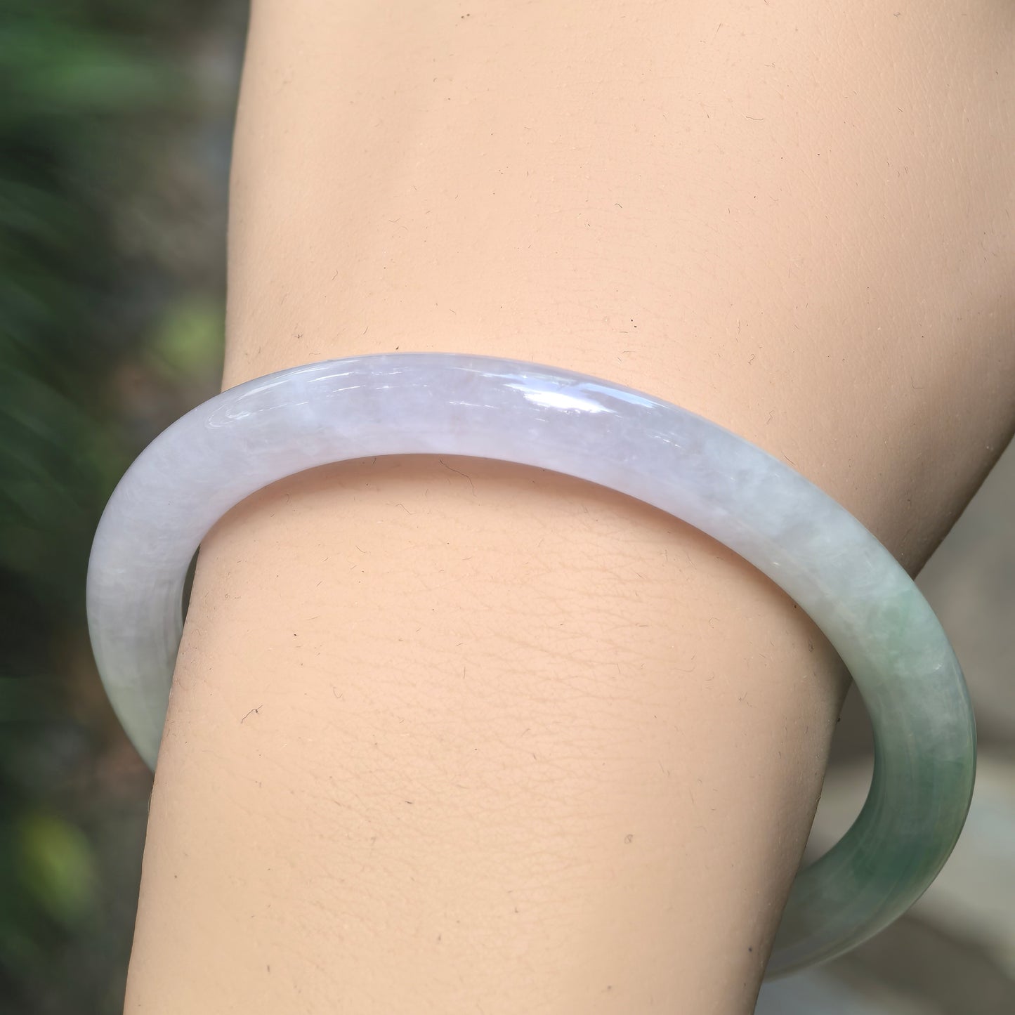 Close wrist view of pale lavender and green Burmese jadeite bangle showing the smooth round profile and natural color transition.