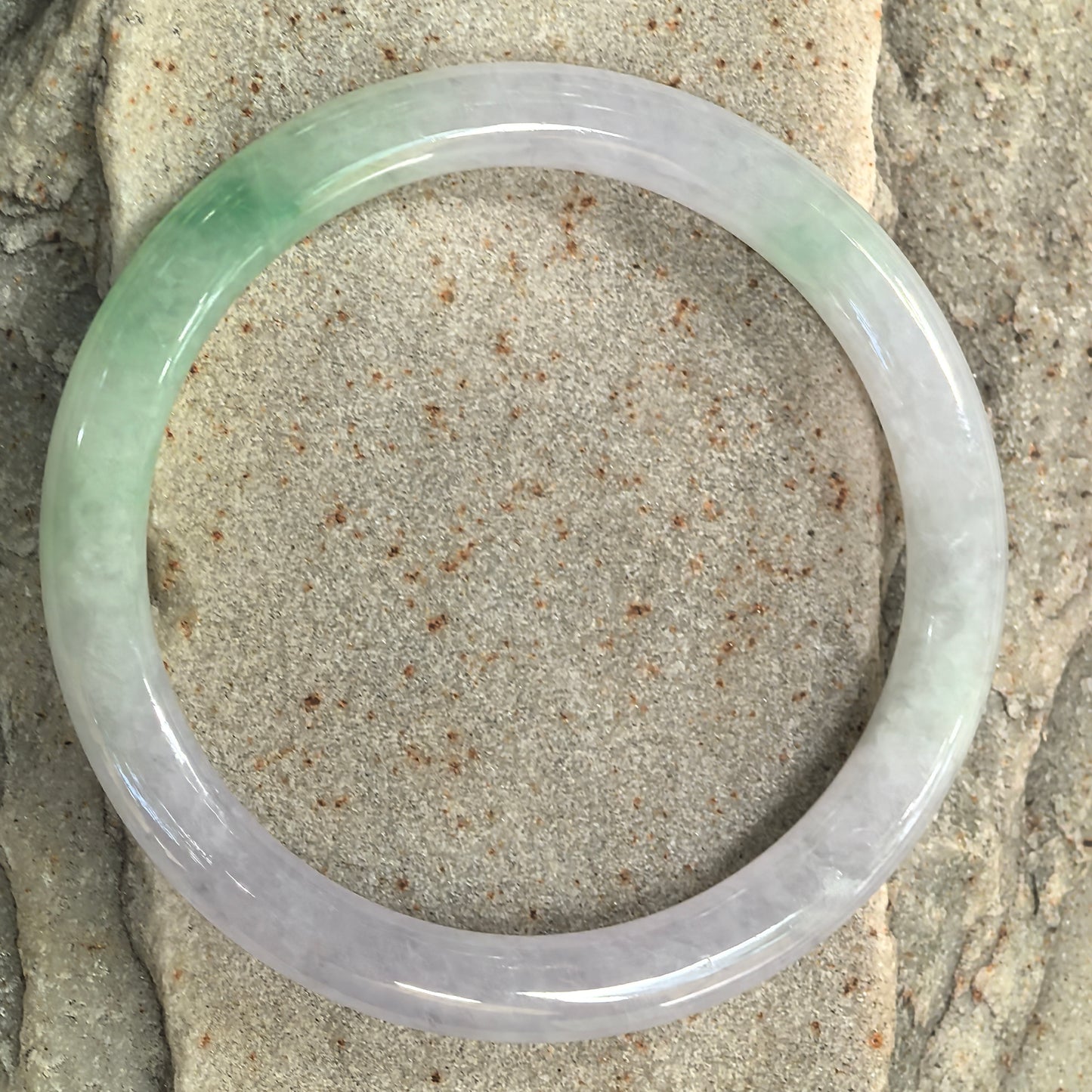 Top view of pale lavender and light green round jadeite bangle showing the natural color distribution and slim proportions.