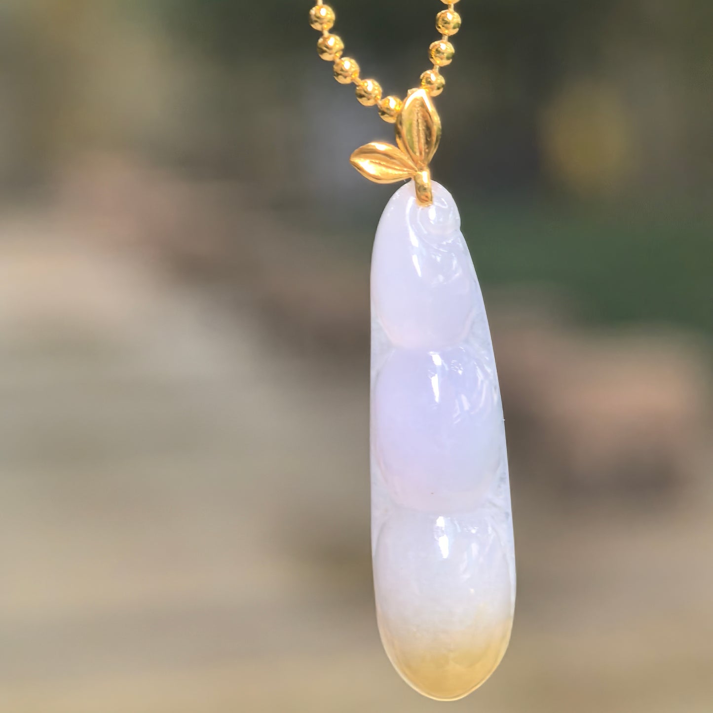 Natural Grade-A pale lavender and yellow jadeite bean pod pendant hanging from a chain with an 18K gold leaf-shaped bail.