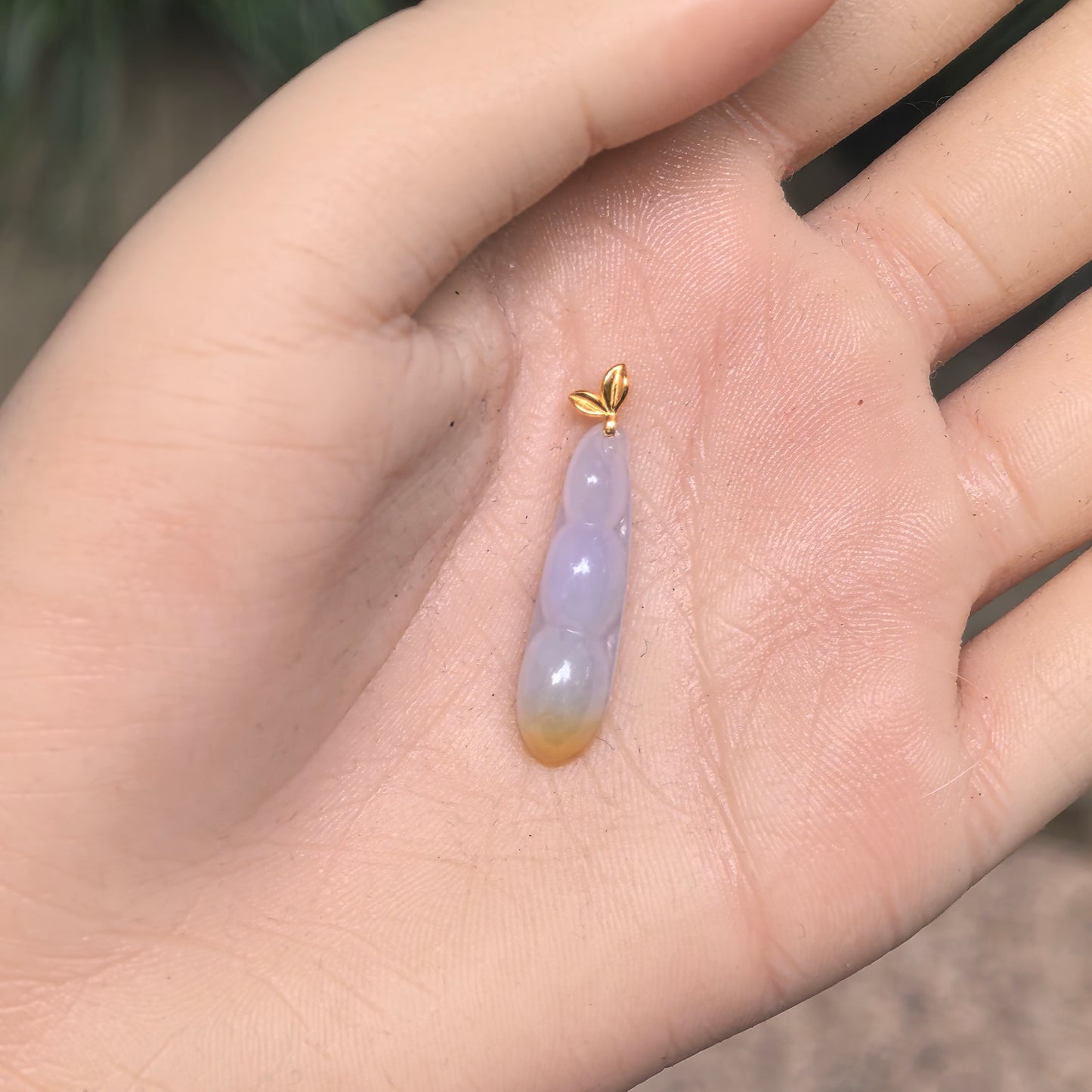 Small icy glutinous lavender and yellow jadeite bean pod pendant shown in hand for scale.