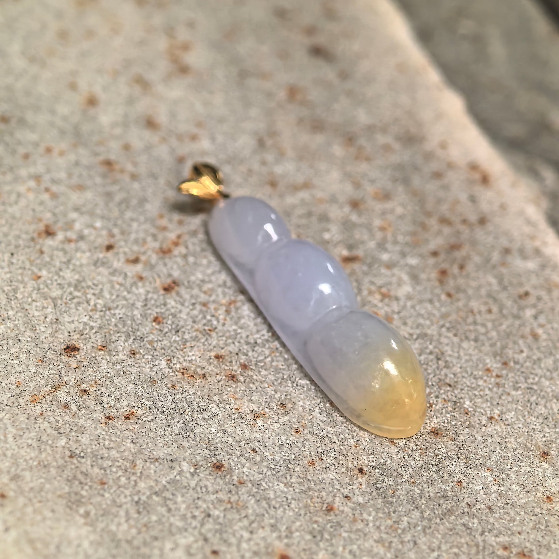 Close-up of pale lavender jadeite bean pod pendant showing the warm yellow tip, smooth carving and polished surface.