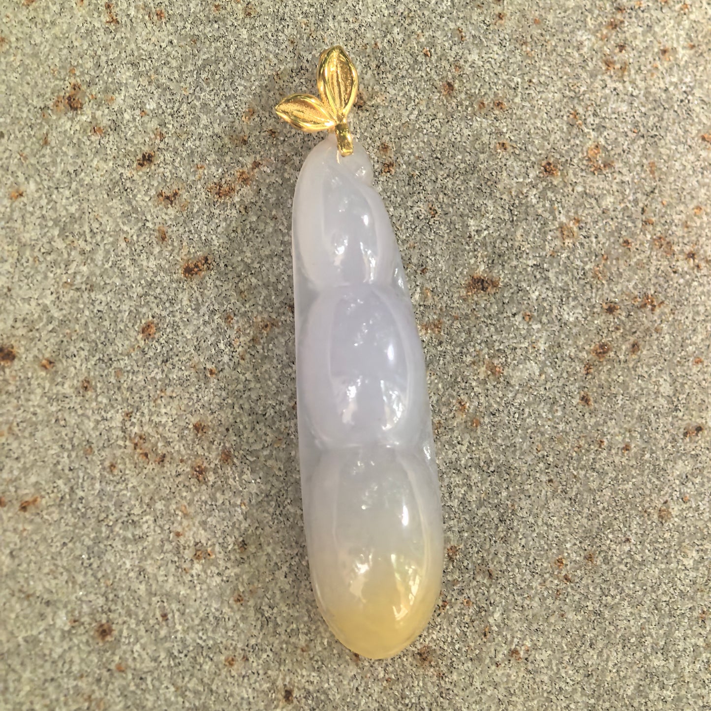 Natural Grade-A lavender and yellow bean pod jadeite pendant displayed on stone with an 18K gold leaf-shaped bail.