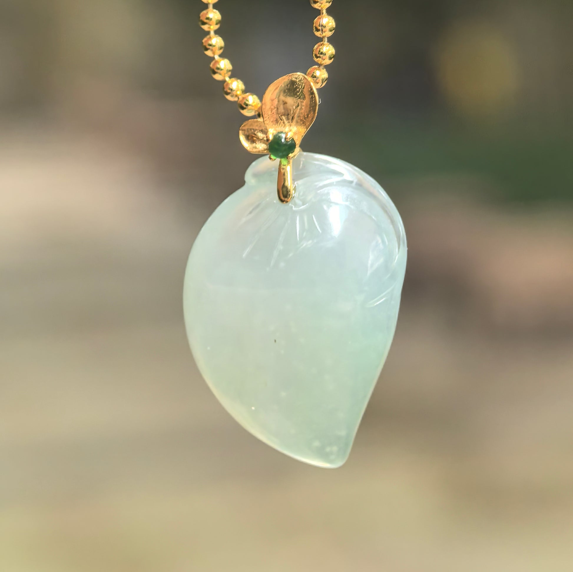 Natural Grade-A icy light green peach jadeite pendant hanging from a chain, showing the polished fruit-shaped carving and 18K gold bail.