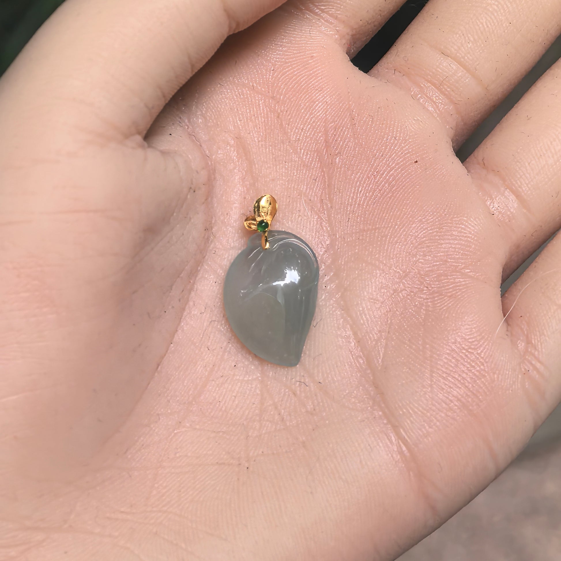 Icy light green peach jadeite pendant with 18K gold bail shown in hand for scale.