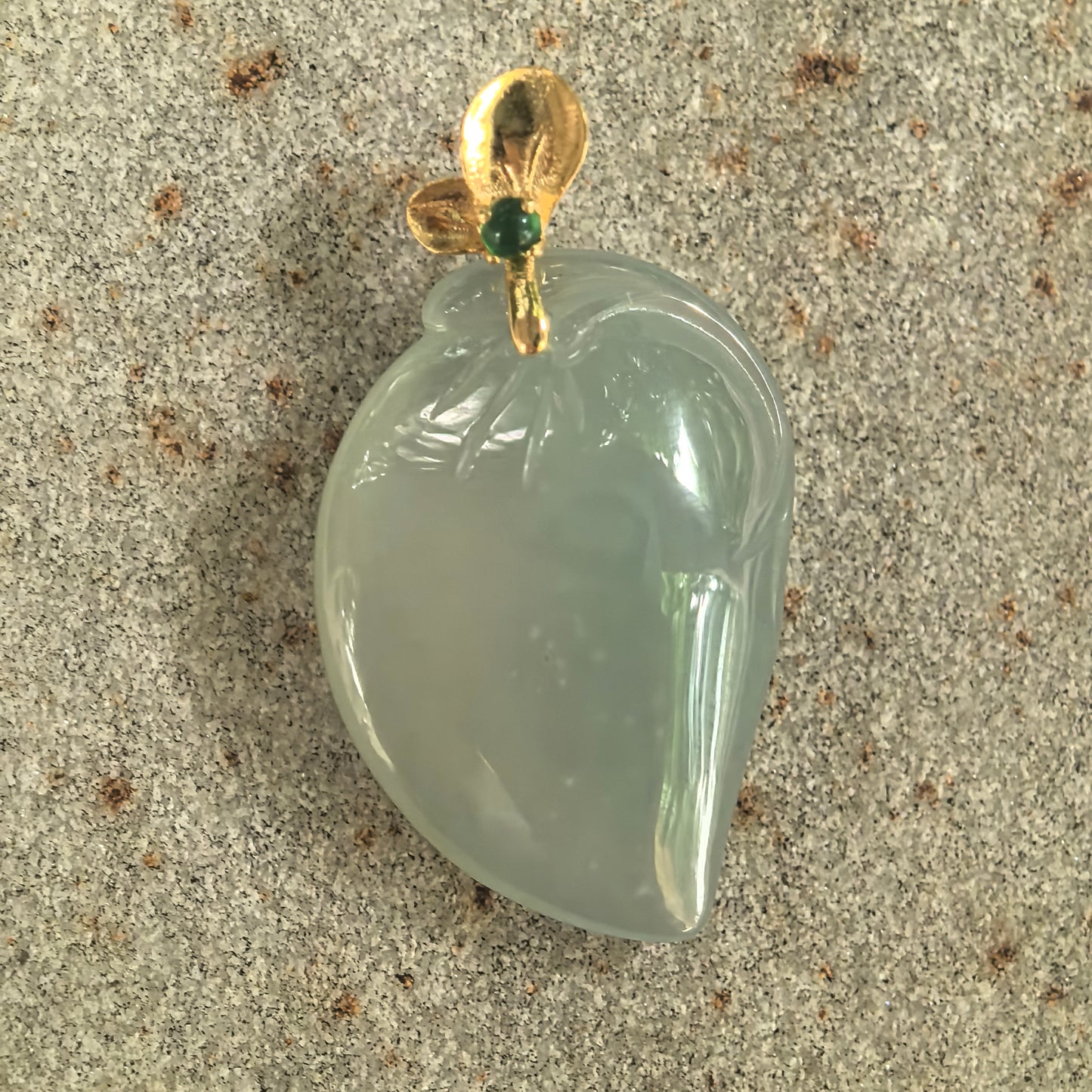 Detailed view of icy light green peach jadeite pendant showing good translucency, rounded carving, and 18K gold bail.