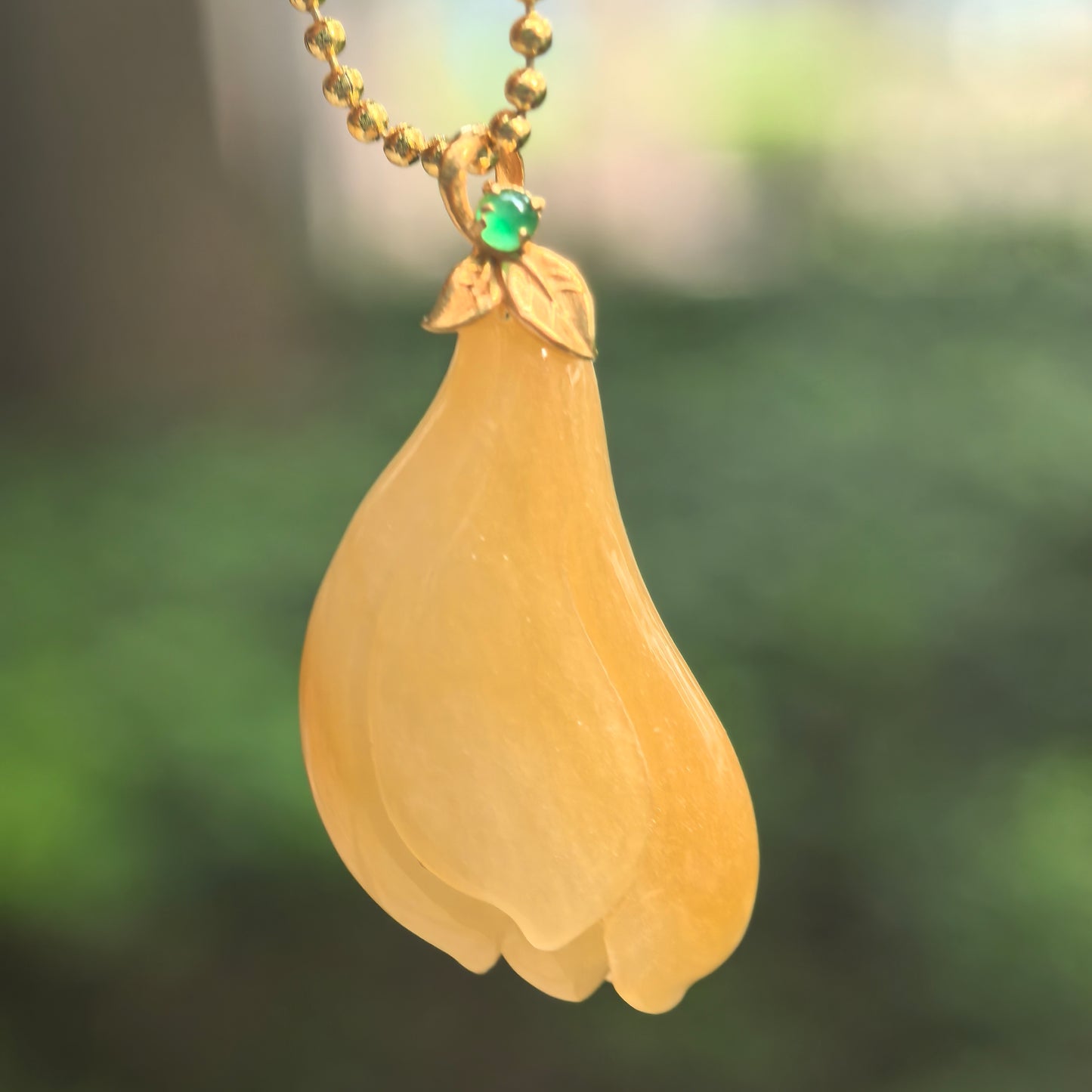 Natural Grade-A icy glutinous yellow magnolia jadeite pendant hanging from a chain with an 18K gold leaf-style bail and green accent stone.