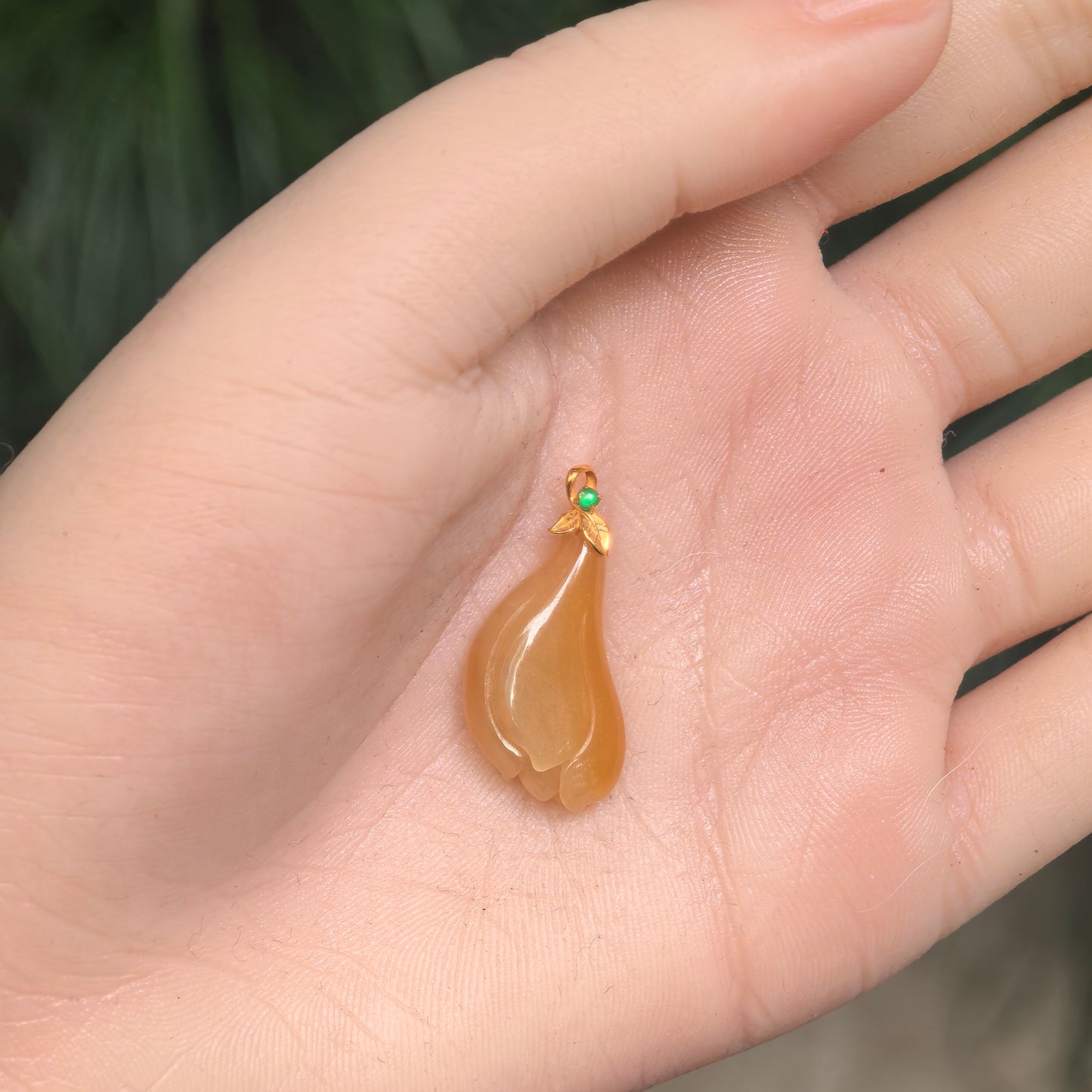 Yellow magnolia jadeite pendant shown in hand for scale with layered flower carving and 18K gold bail.