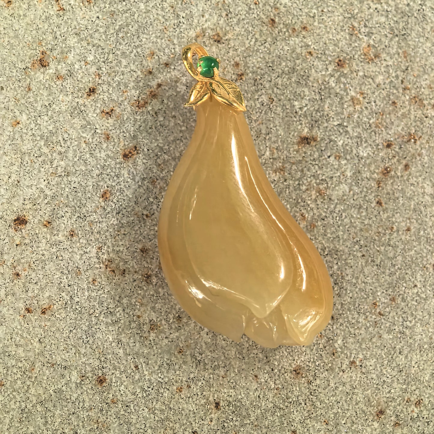 Natural Grade-A yellow magnolia jadeite pendant displayed on stone with an 18K gold leaf-style bail and green accent stone.