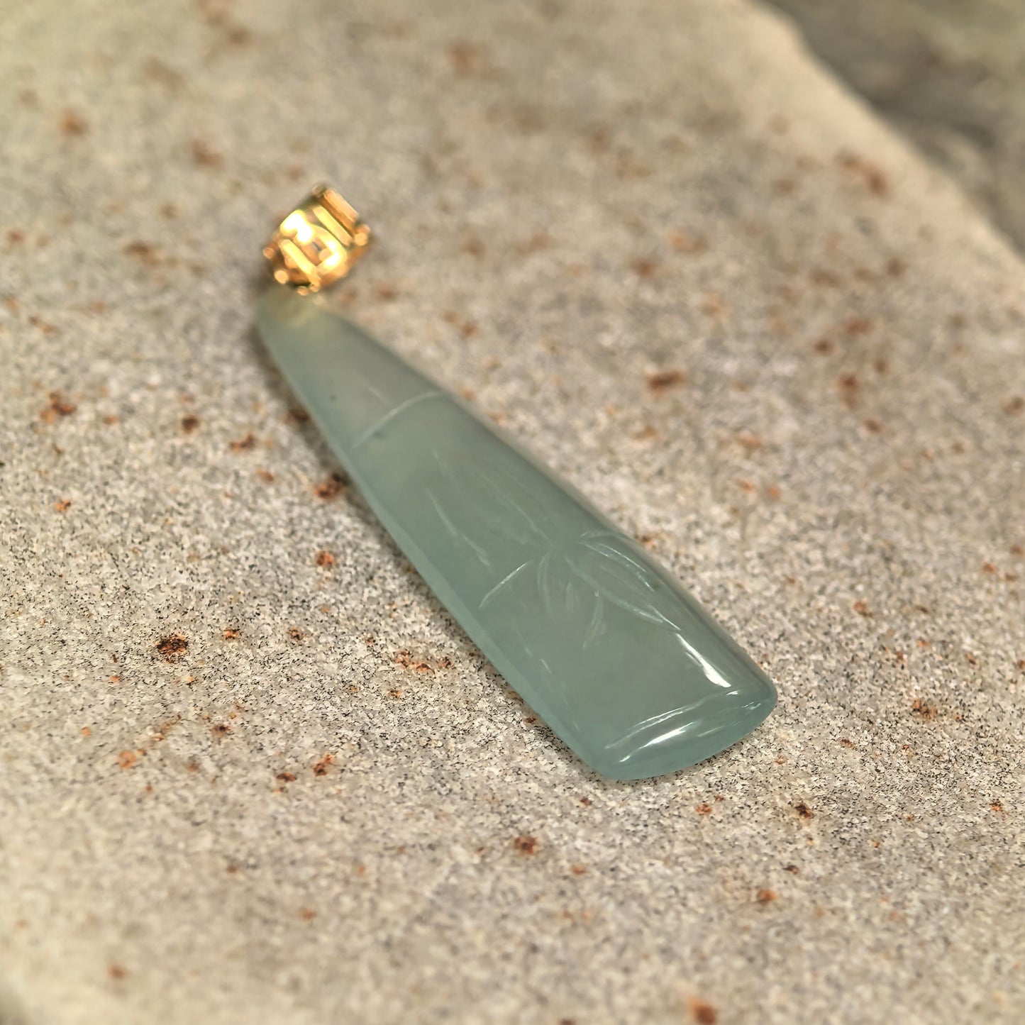 Close-up of light green bamboo jadeite pendant showing good translucency, polished surface, and carved bamboo leaf details.