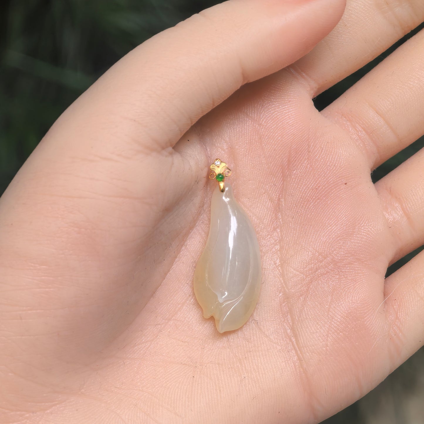 Natural Grade-A pale yellow magnolia jadeite pendant shown in hand for scale with layered floral carving and 18K gold bail.