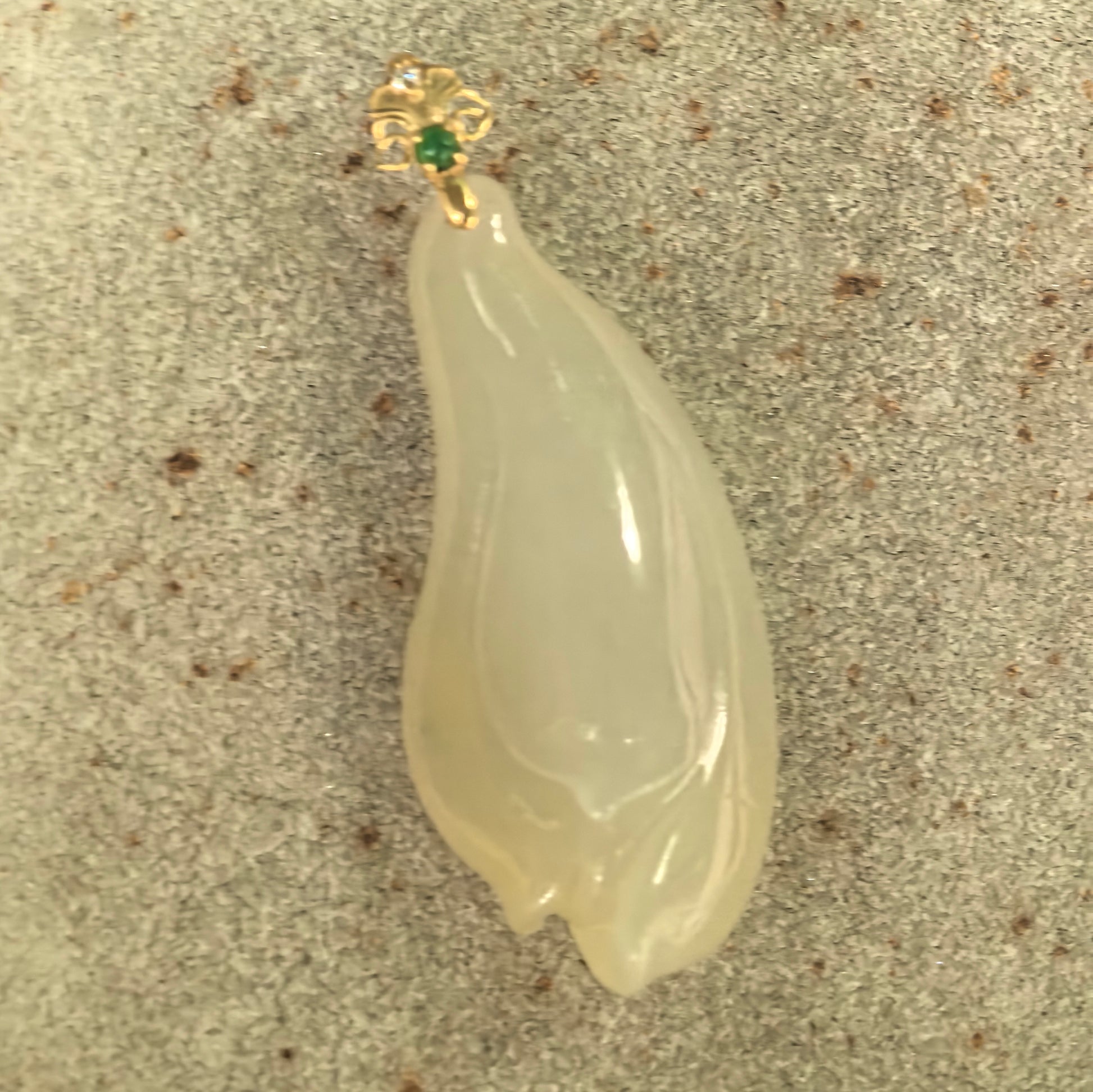 Natural Grade-A pale yellow magnolia jadeite pendant displayed on stone showing its elongated floral shape and 18K gold setting.