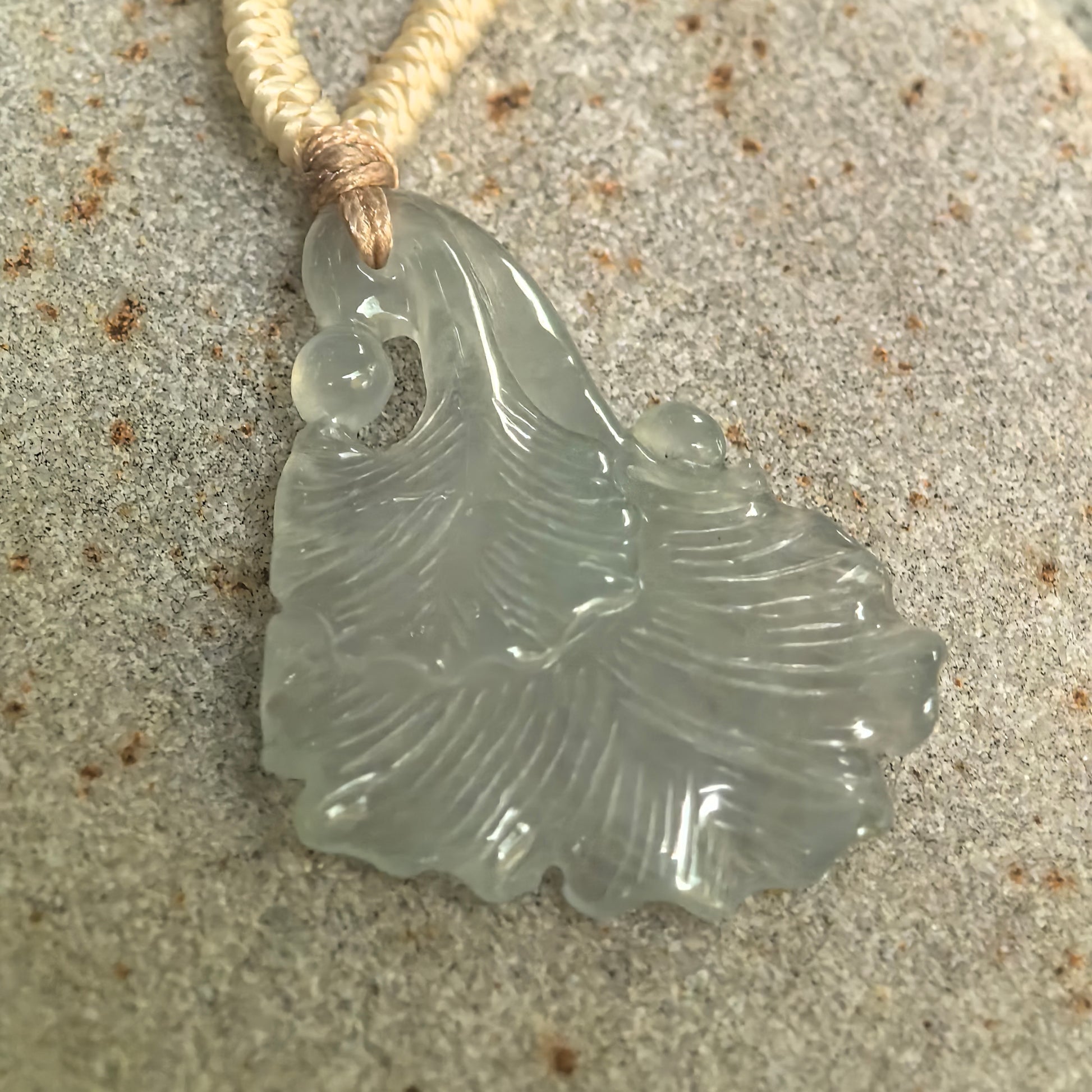 Angled detail of icy light green ginkgo leaf jadeite pendant showing polished carving, translucent material and scalloped leaf edge.