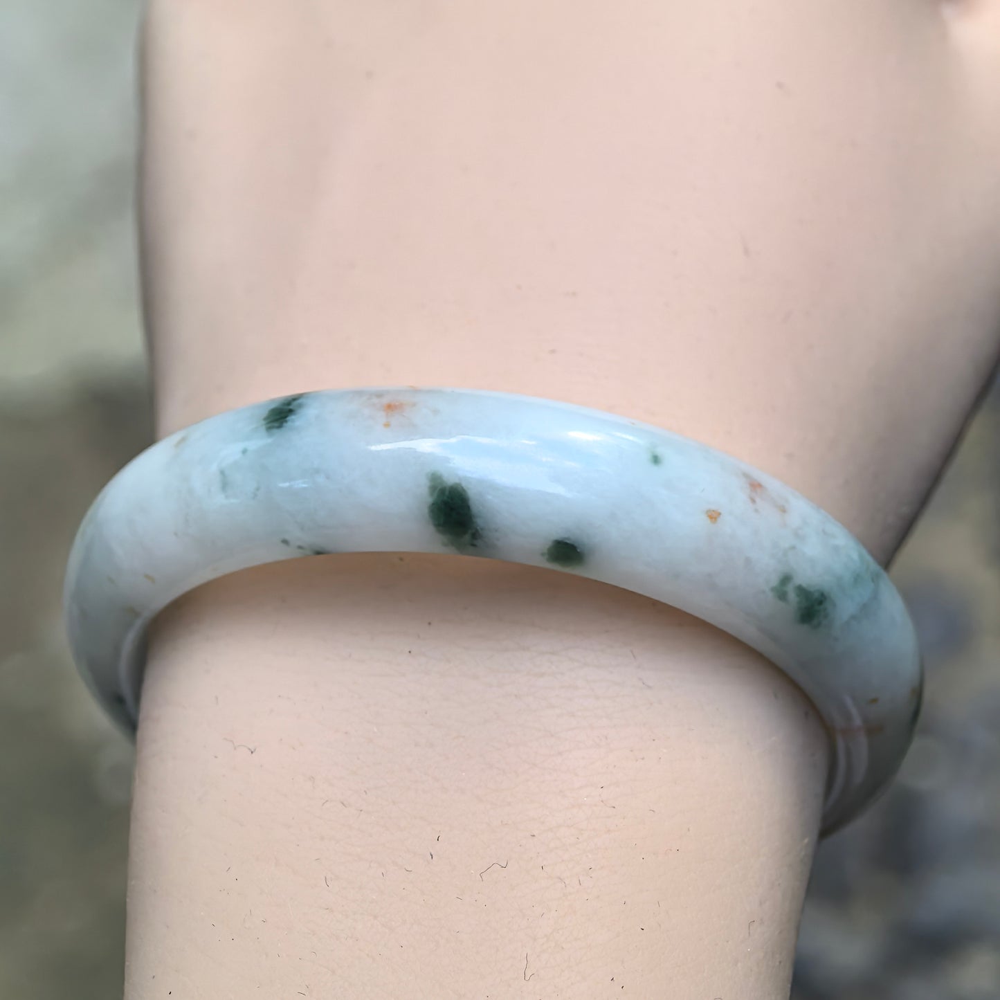 Close-up wrist view of fine glutinous milk white Burmese jadeite bangle showing green floating flowers, golden flecks, and smooth polished texture.