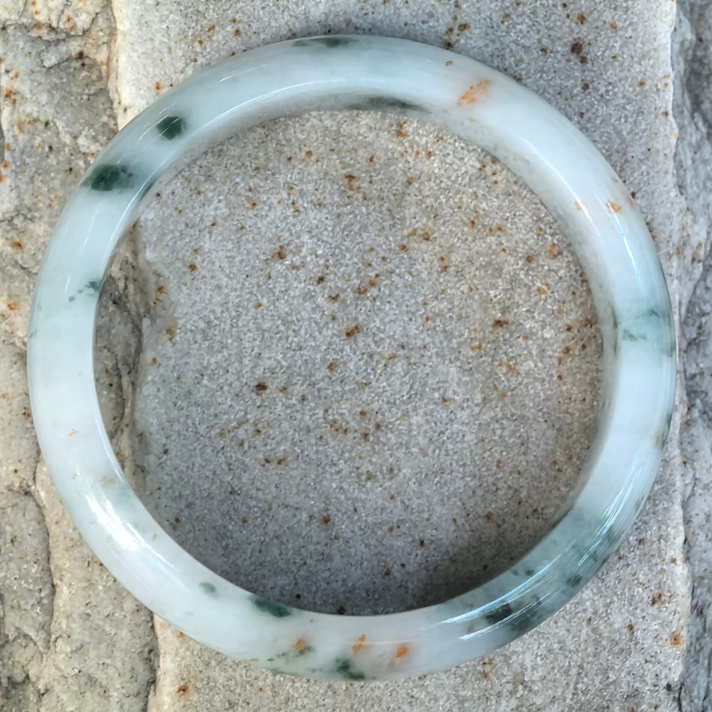 Top view of NGTC certified milk white Burmese jadeite D-shape bangle showing scattered dark green floating flowers and distinctive golden-brown flecks.