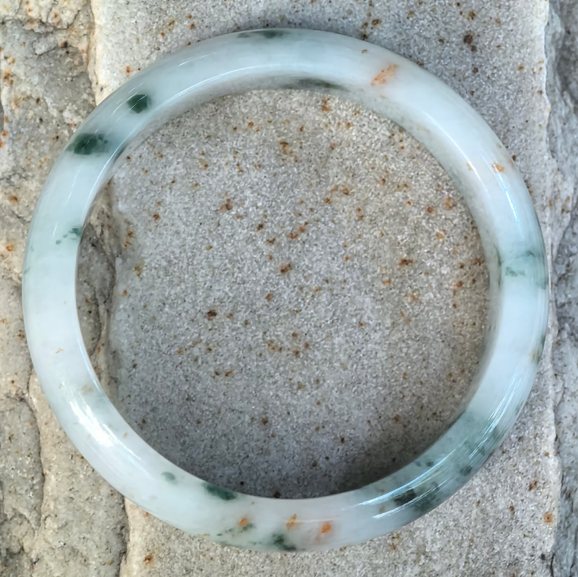 Top view of NGTC certified milk white Burmese jadeite D-shape bangle showing scattered dark green floating flowers and distinctive golden-brown flecks.