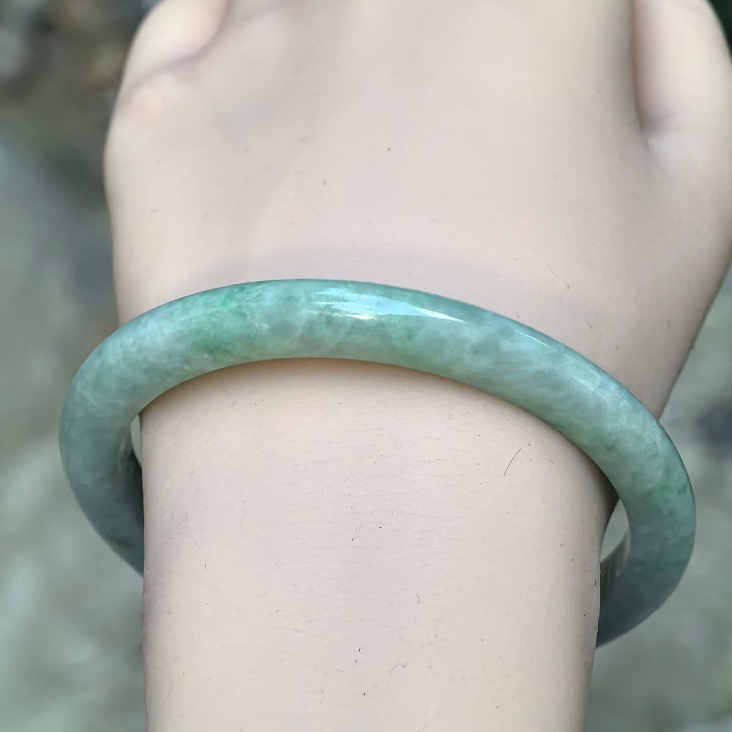 Wrist view of bean-glutinous apple green Burmese jadeite bangle showing its polished surface and delicate D-shape profile.