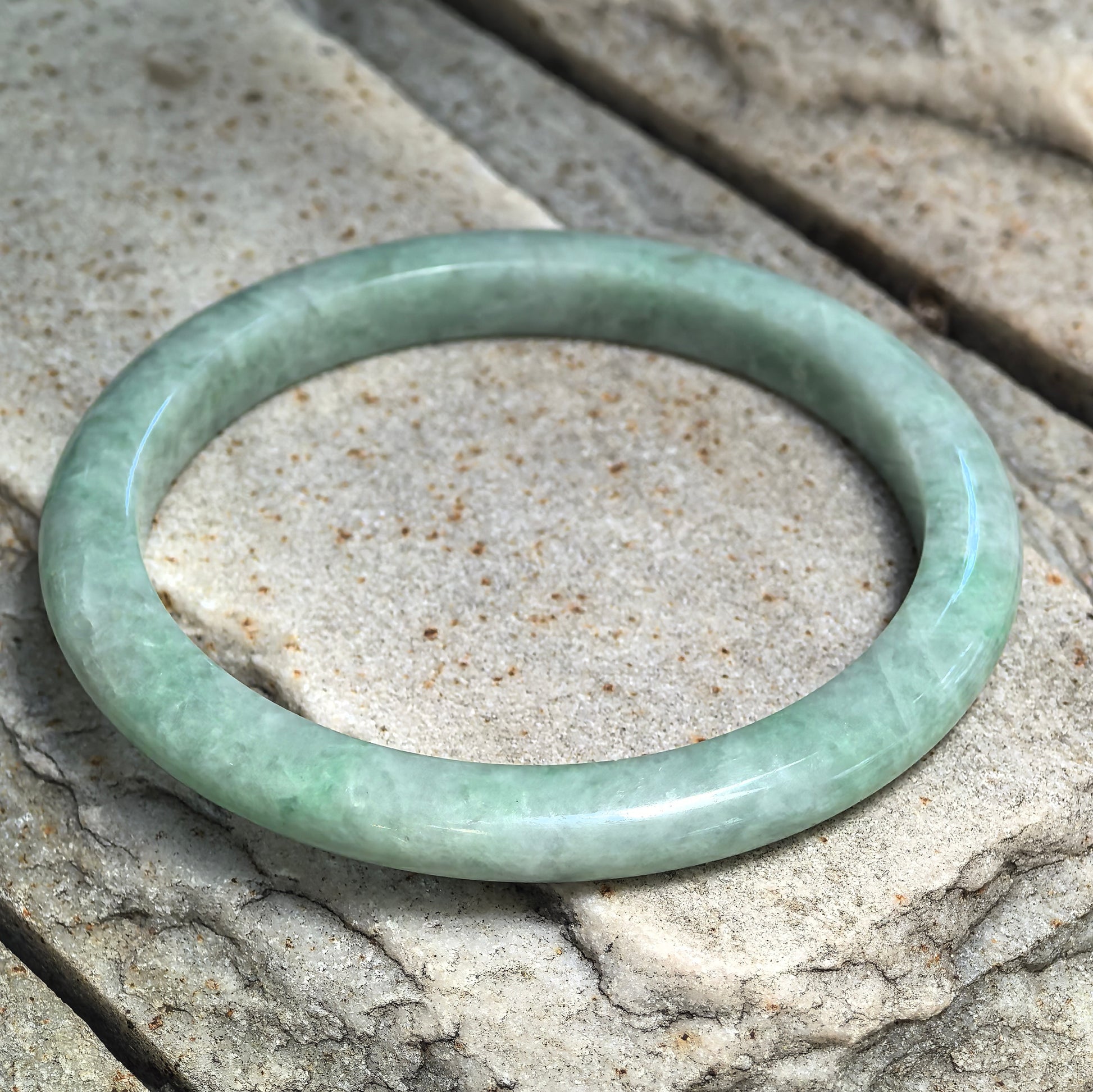 Natural Grade-A apple green jadeite D-shape bangle displayed on stone showing the bean-glutinous texture and soft natural green variations.