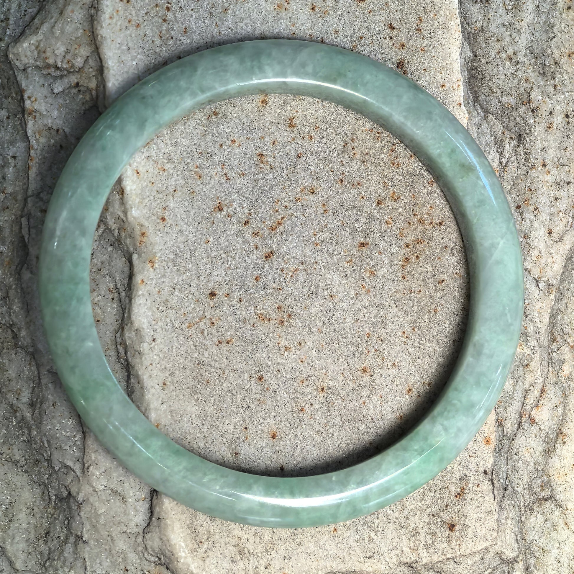 Top view of slim apple green Burmese jadeite D-shape bangle showing the even circular form, polished finish, and natural mottled texture.