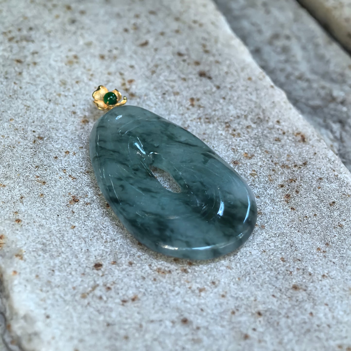 Close-up of dark ink green Burmese jadeite spiral pendant on stone showing the flowing carved structure, central opening, and smooth polished luster.