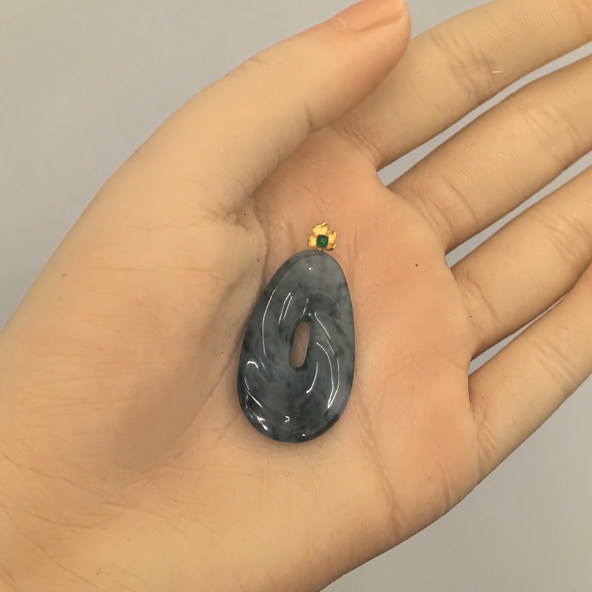 Hand-held view of dark ink green icy glutinous Burmese jadeite spiral pendant showing its elongated central opening and polished curved form.