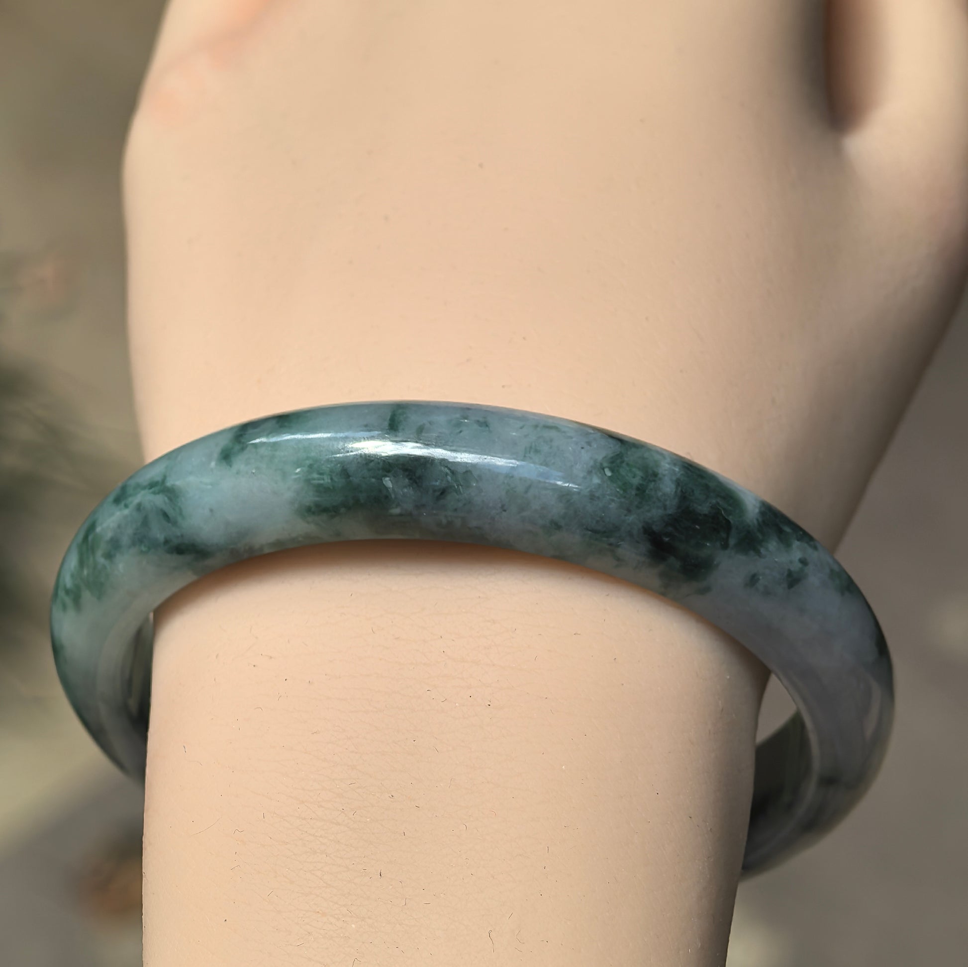 Close-up wearing view of dark green floating flower jadeite D-shape bangle showing natural mottled color distribution and polished luster.