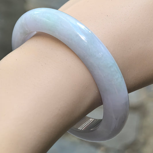 Glutinous pale lavender and light green Burmese jadeite D-shape bangle worn on the wrist in natural light.