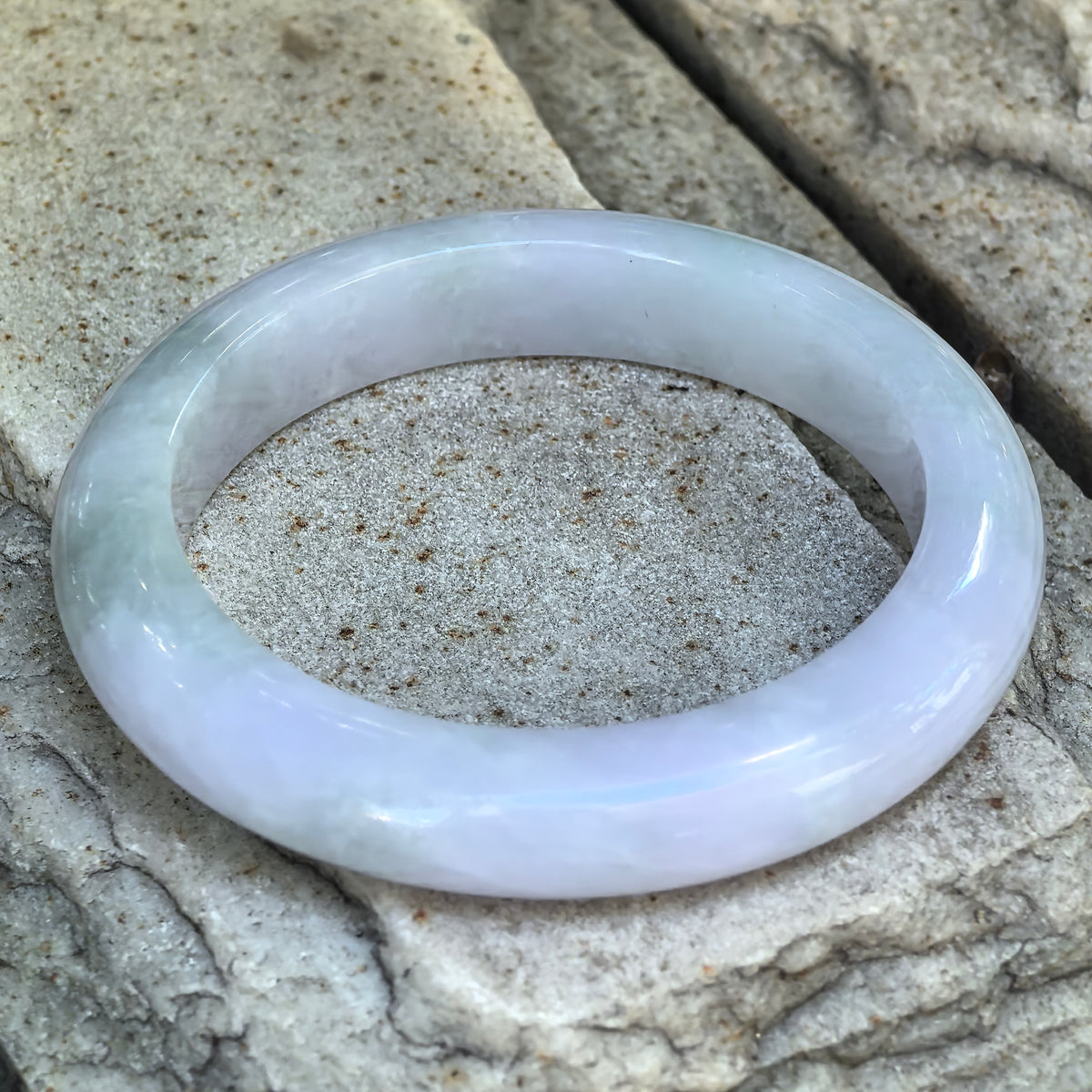Glutinous pale lavender and light green Burmese jadeite D-shape bangle displayed at an angle on a stone surface.