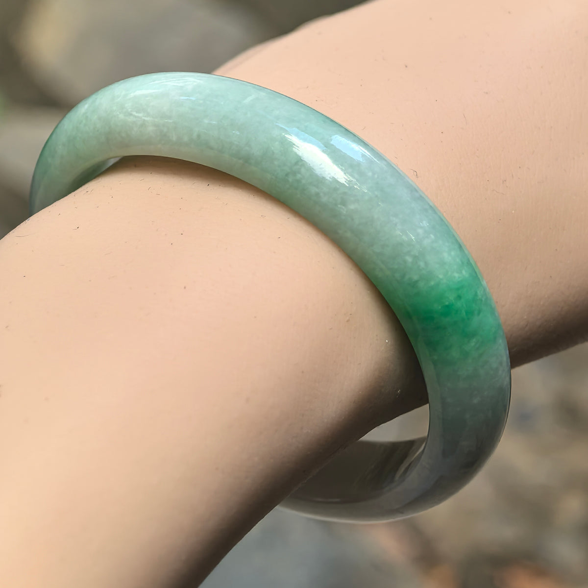 White-base green Burmese jadeite oval bangle worn on the wrist showing glutinous texture and vivid green accent.