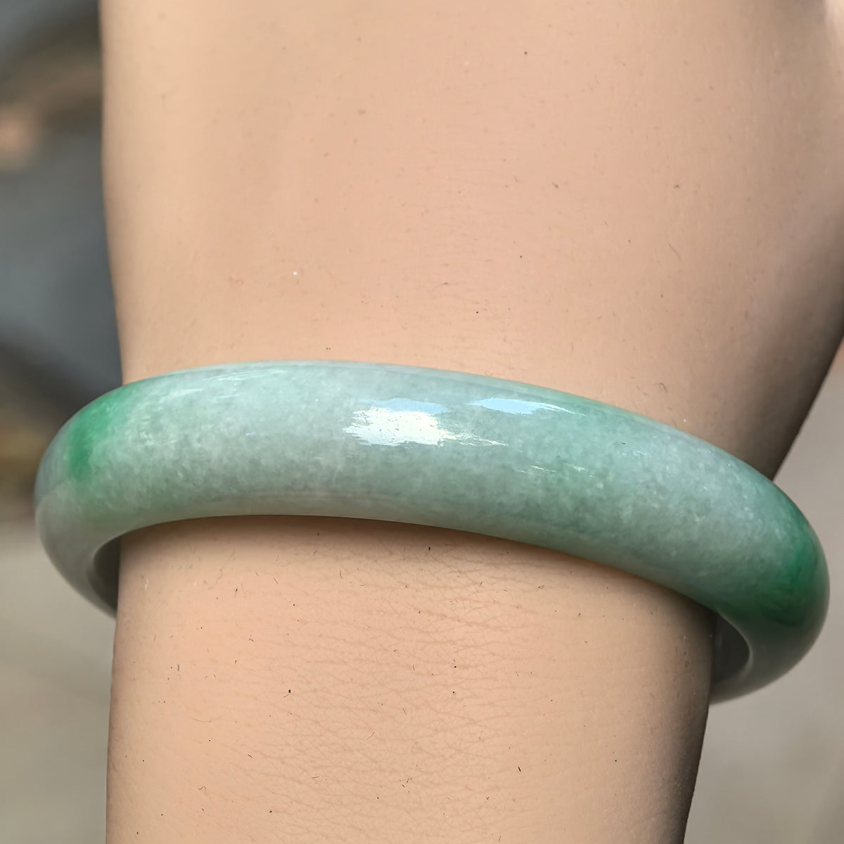Natural Grade-A white-base green jadeite bangle worn on the wrist showing its smooth oval profile and polished luster.