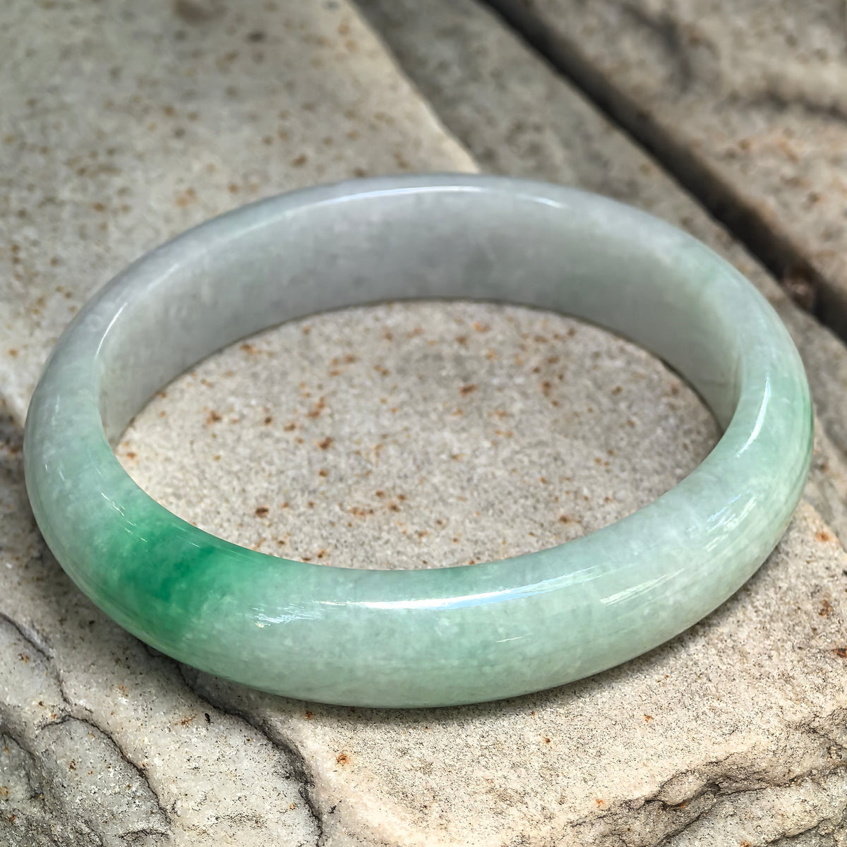 Glutinous white-base green oval jadeite bangle displayed at an angle showing soft translucency and concentrated green color.