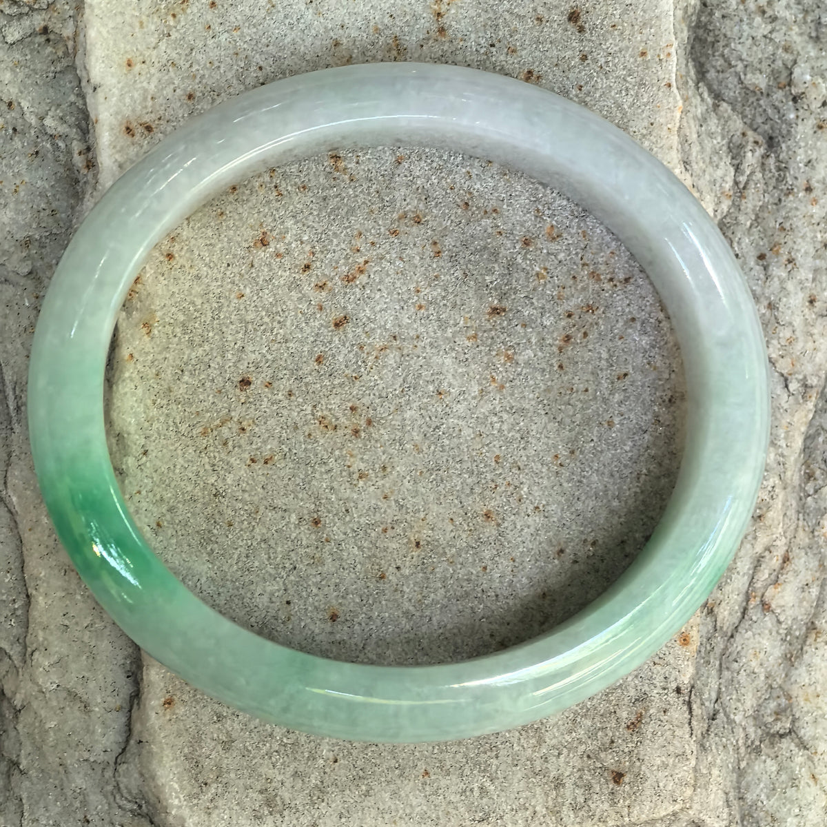 Natural Grade-A glutinous white-base green oval jadeite bangle shown from above with concentrated green color along one section.