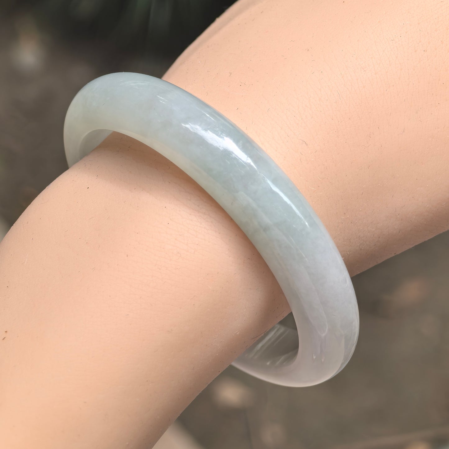 Angled wrist close-up of a light green fine glutinous jadeite D-shape bangle, showing its rounded outer surface and polished luster.
