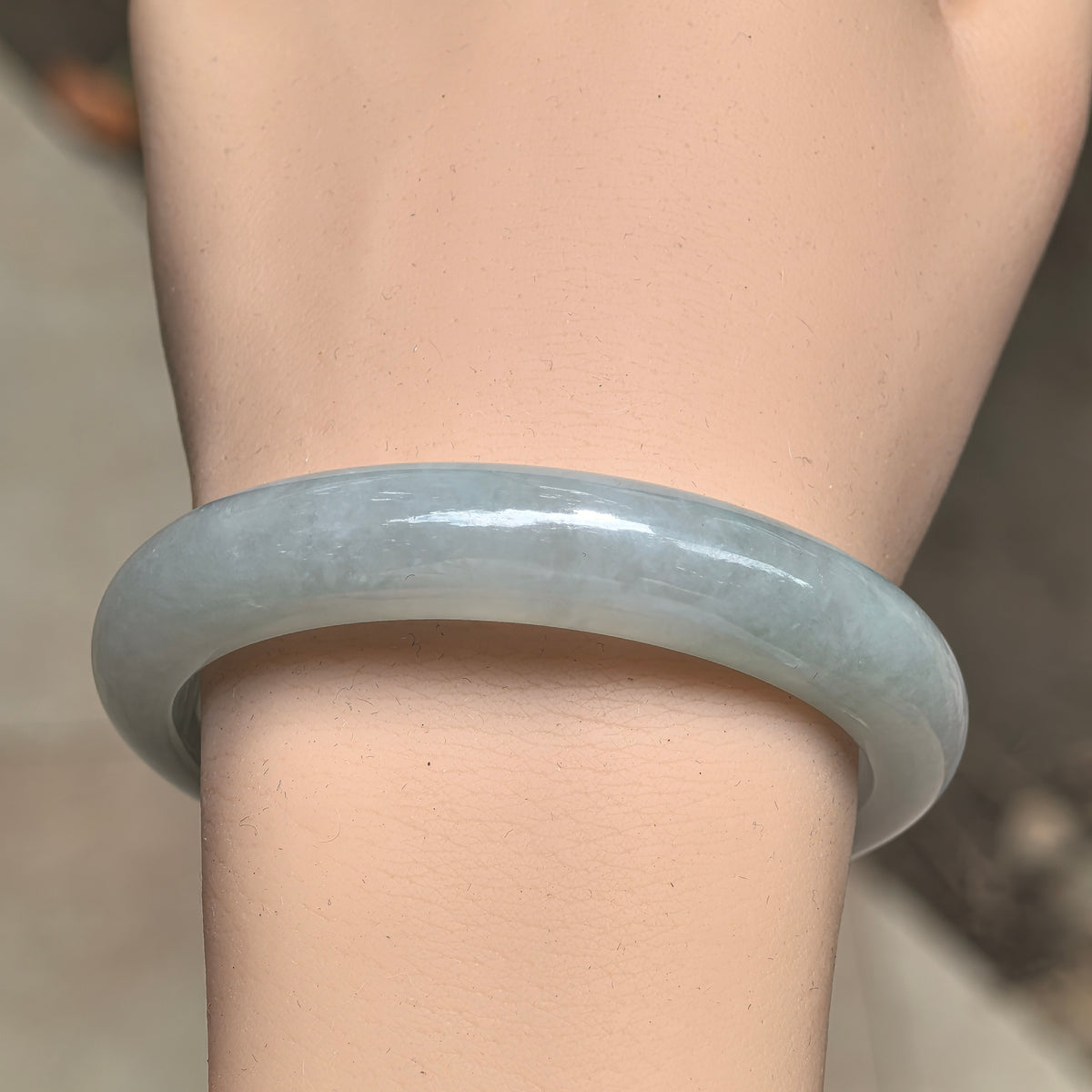 Front wrist view of a pale green jadeite D-shape bangle with delicate internal texture and soft color variations.