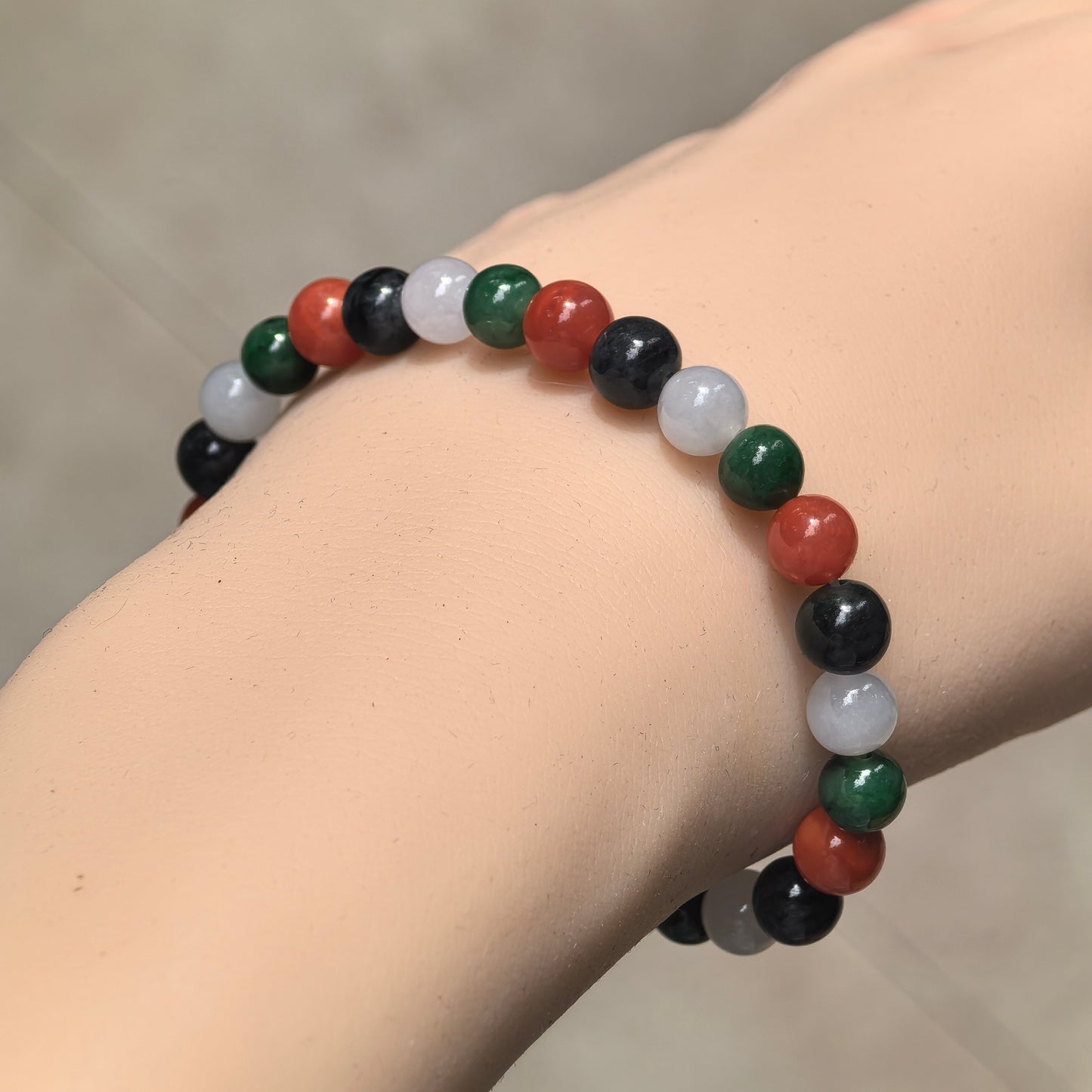 Multicolor jadeite and Nanhong agate bead bracelet worn on the wrist, showing the repeating red, green, white and black color arrangement.