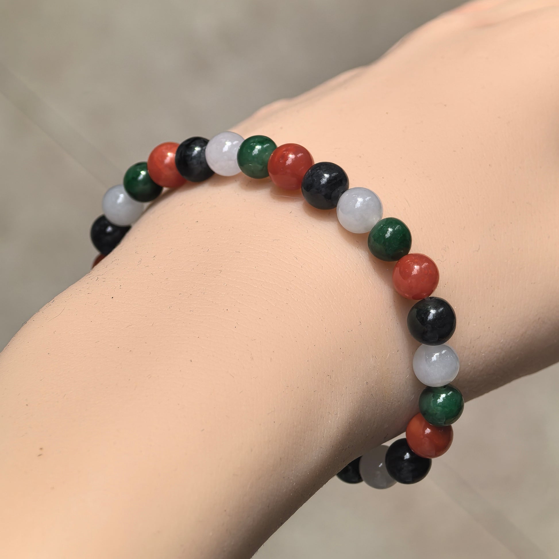Multicolor jadeite and Nanhong agate bead bracelet worn on the wrist, showing the repeating red, green, white and black color arrangement.