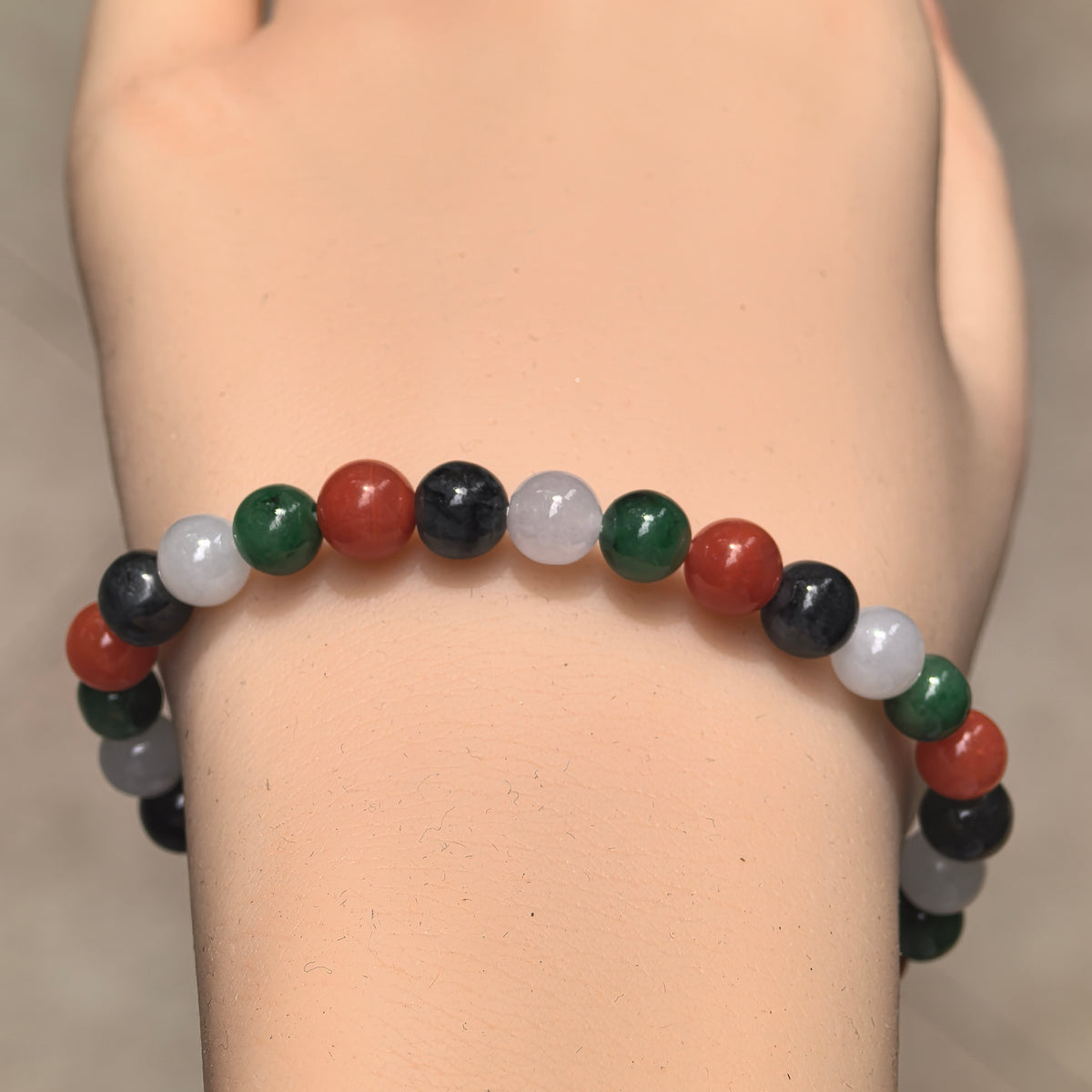 Wrist view of Natural Grade-A glutinous jadeite bead bracelet with green, white and black jadeite and red Nanhong agate beads.
