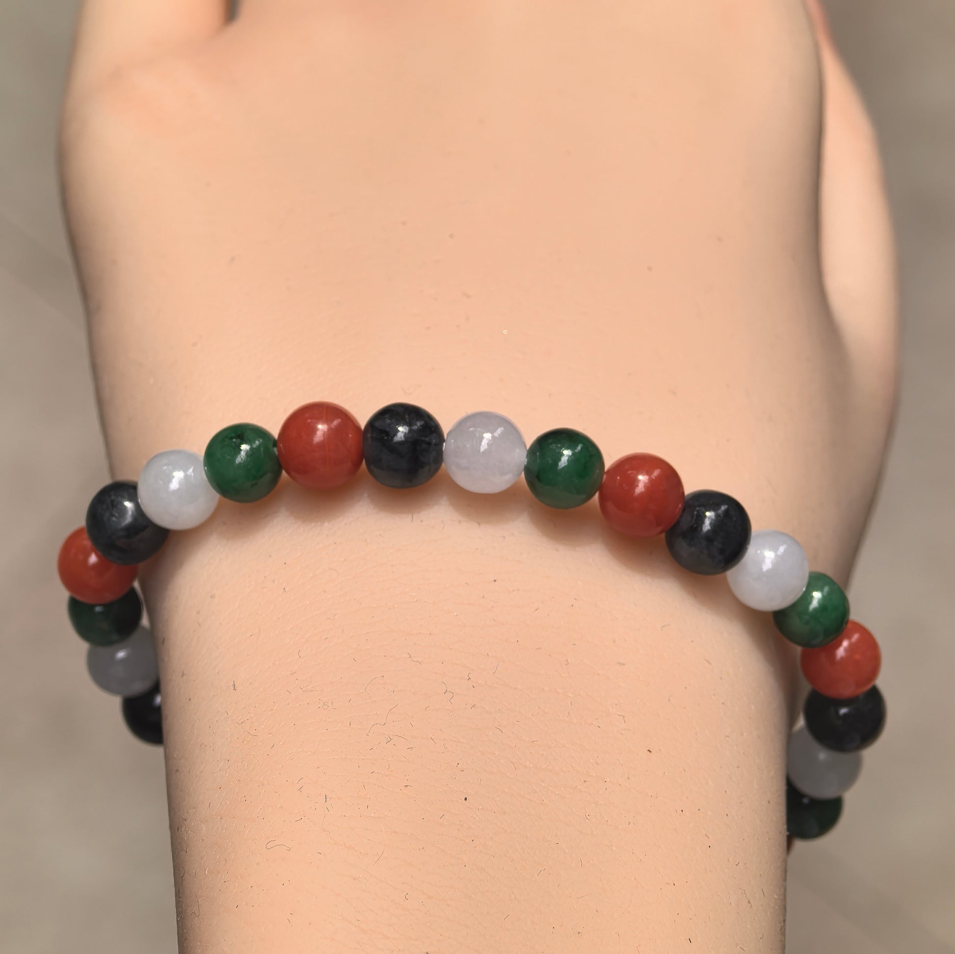 Wrist view of Natural Grade-A glutinous jadeite bead bracelet with green, white and black jadeite and red Nanhong agate beads.