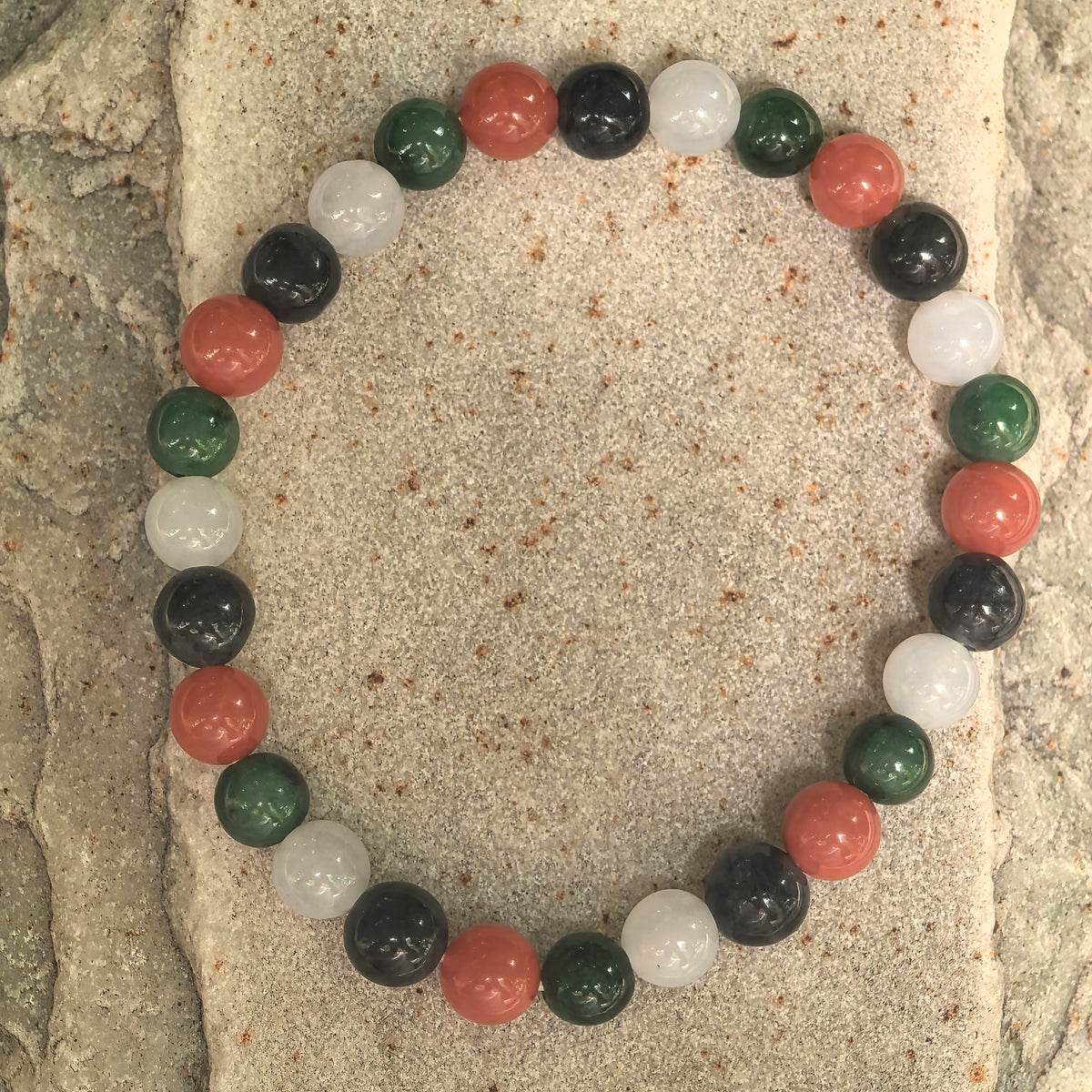 Full top view of the 28-bead multicolor bracelet showing NGTC-certified jadeite beads in green, white and black with red Nanhong agate beads.