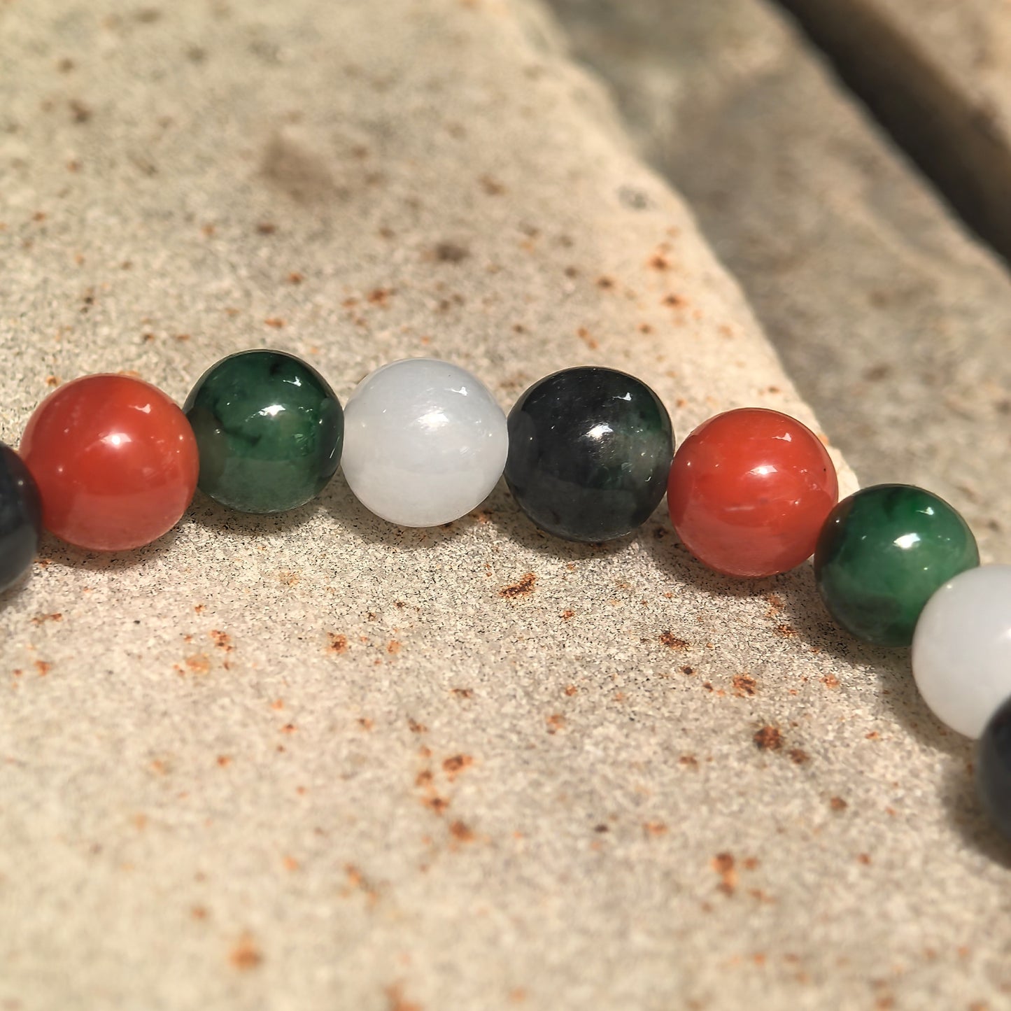Close-up of multicolor bracelet with NGTC-certified green, white and black jadeite beads and contrasting red Nanhong agate beads.
