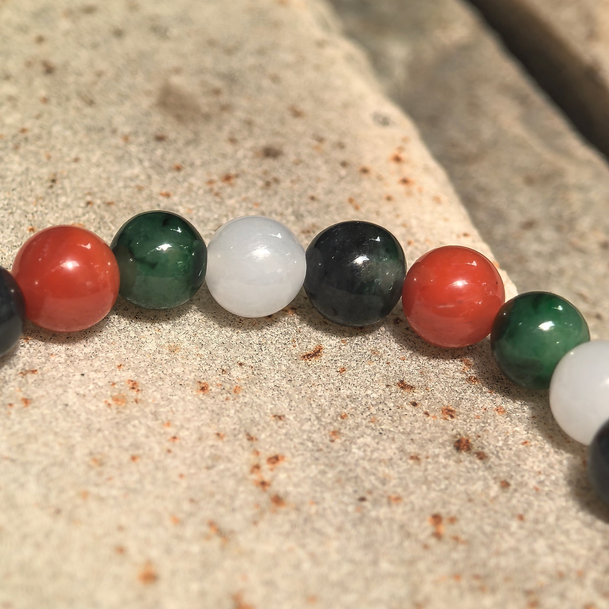 Close-up of multicolor bracelet with NGTC-certified green, white and black jadeite beads and contrasting red Nanhong agate beads.