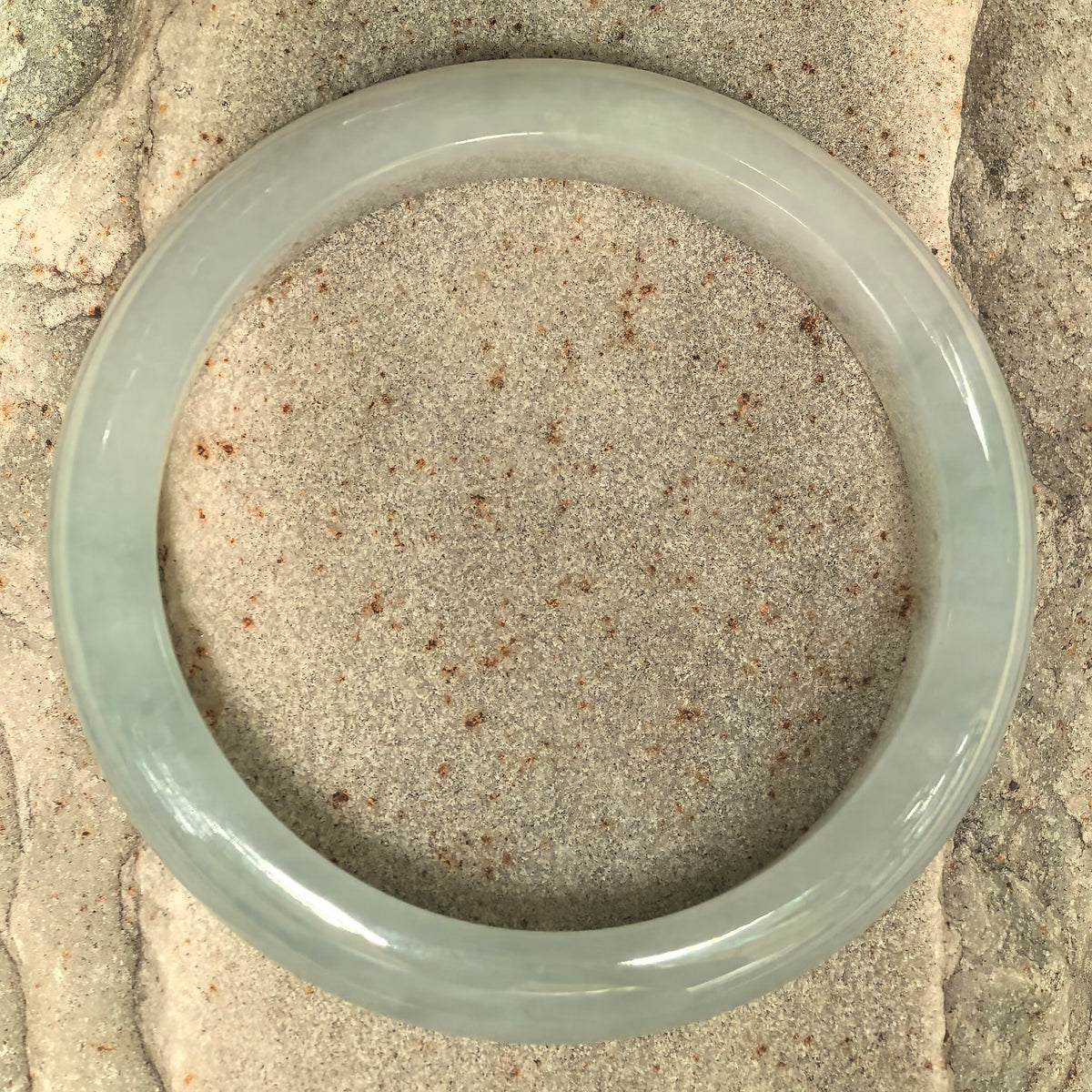 Top view of a light green fine glutinous jadeite bangle on stone, showing its circular shape and subtle variations in color.