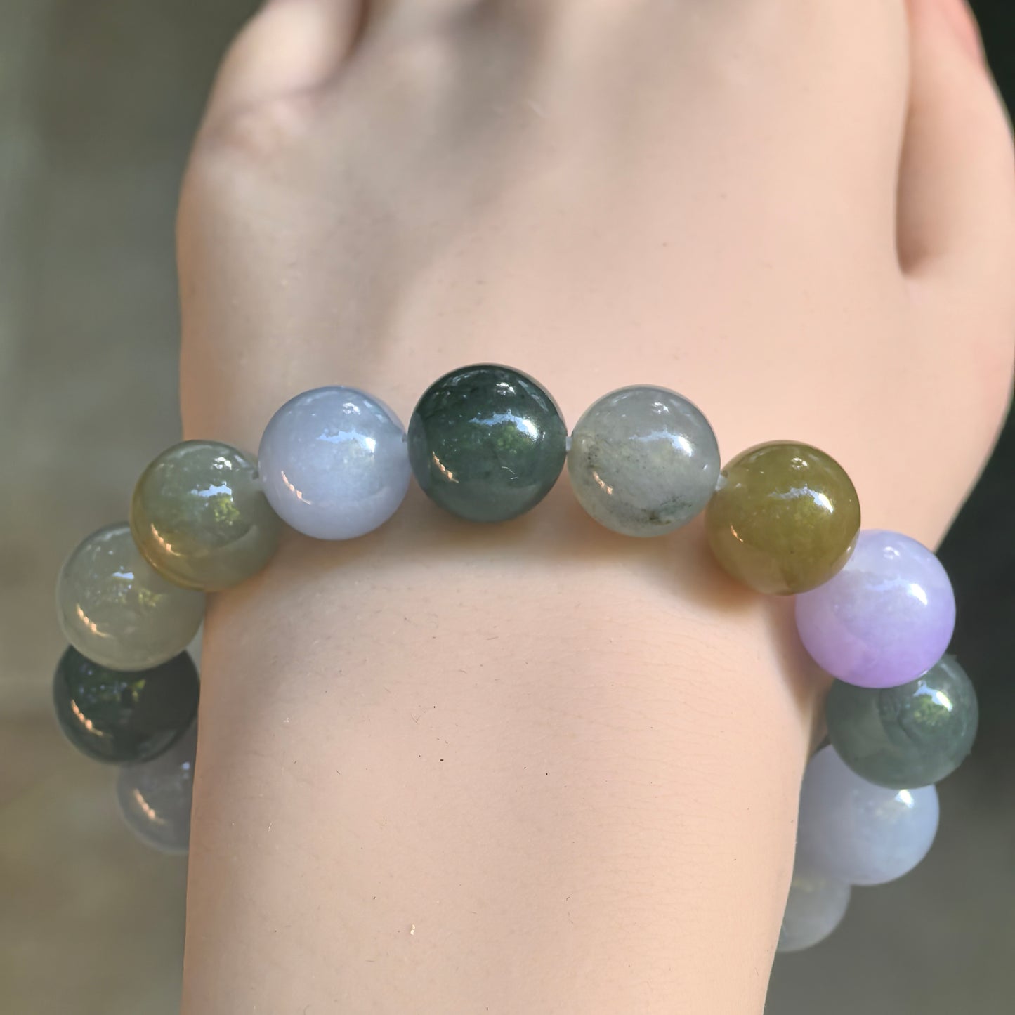 Front wrist view of a round-bead jadeite bracelet showing the contrast between pale lavender, deep green, gray-green, and yellow-brown colors.