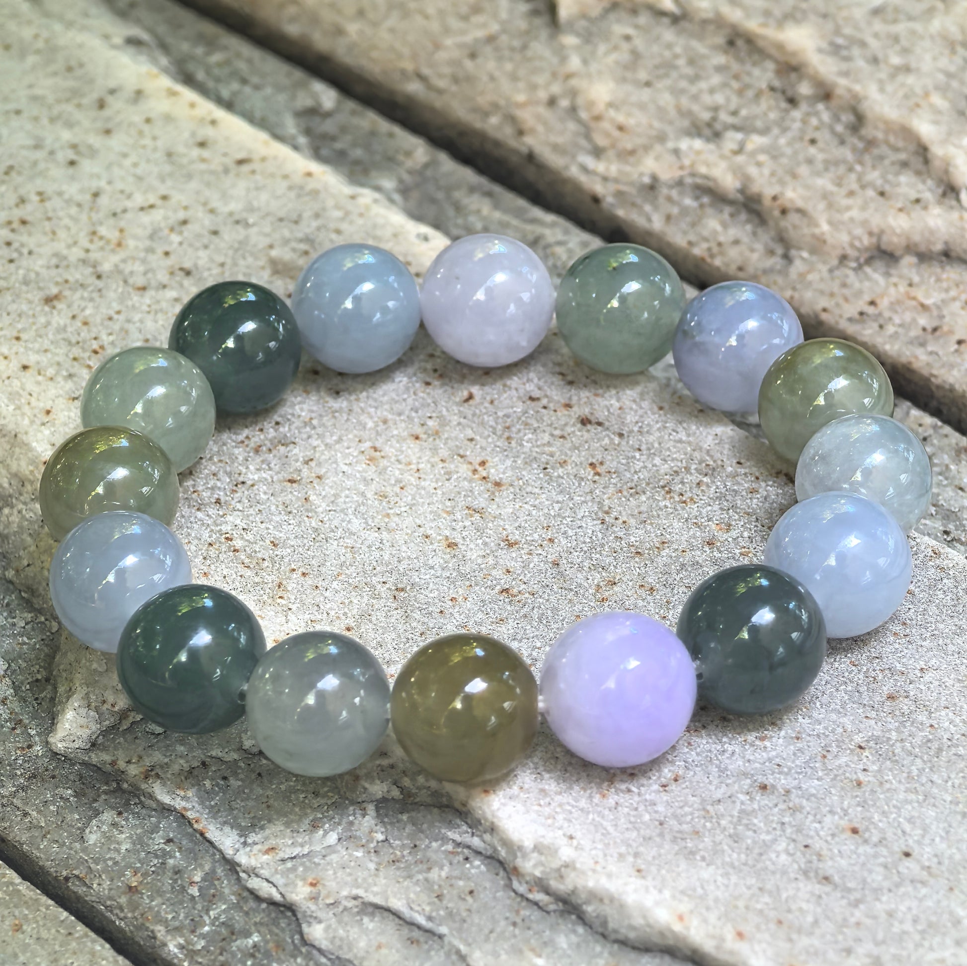 Angled view of the lavender, green, and yellow-brown jadeite bracelet on stone, highlighting rounded beads, cloudy inclusions, and visible bead lines.