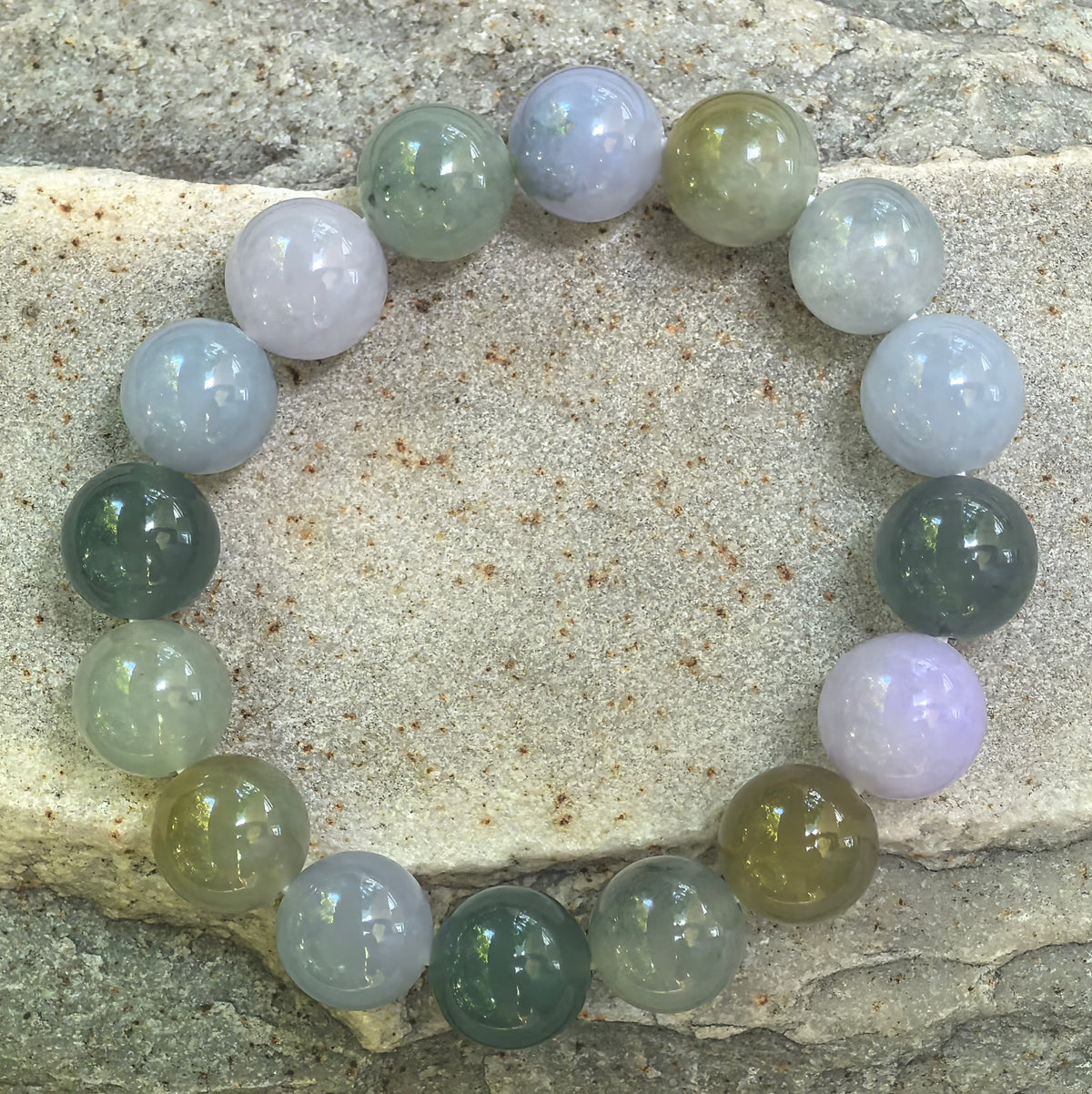 Top view of the multicolor glutinous jadeite bracelet arranged in a complete circle on stone, showing all sixteen polished round beads.