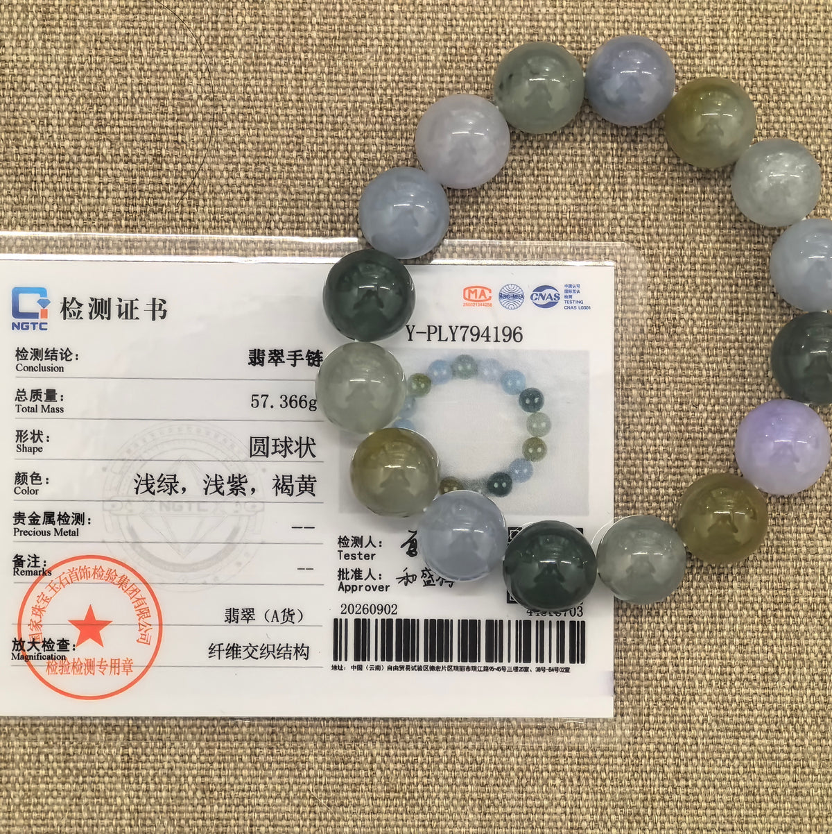 Multicolor jadeite bead bracelet displayed on woven fabric with its matching NGTC certificate identifying the material as Grade-A jadeite.