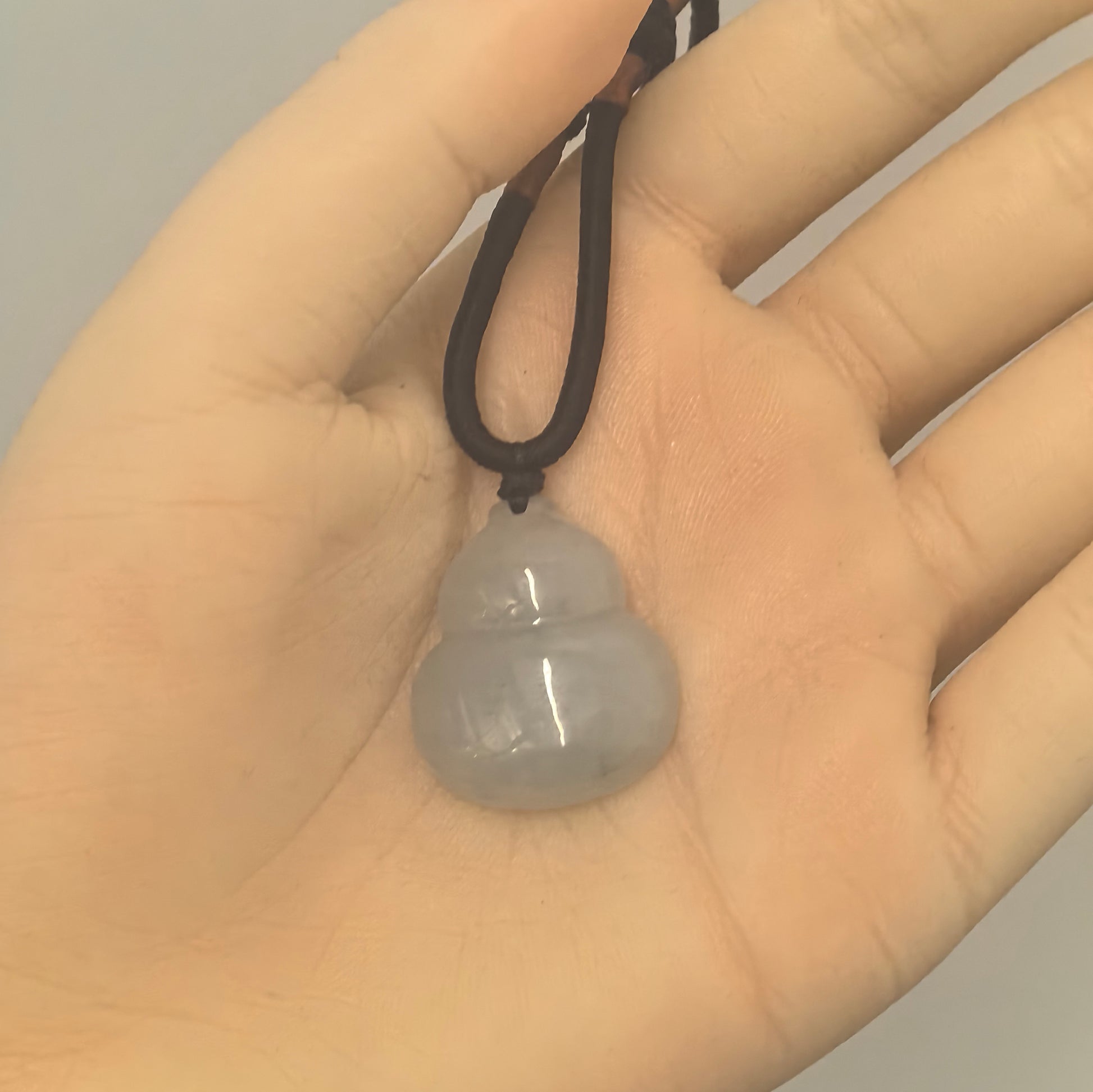 Light green jadeite gourd pendant on a black cord resting in an open palm, showing its rounded shape and polished surface.
