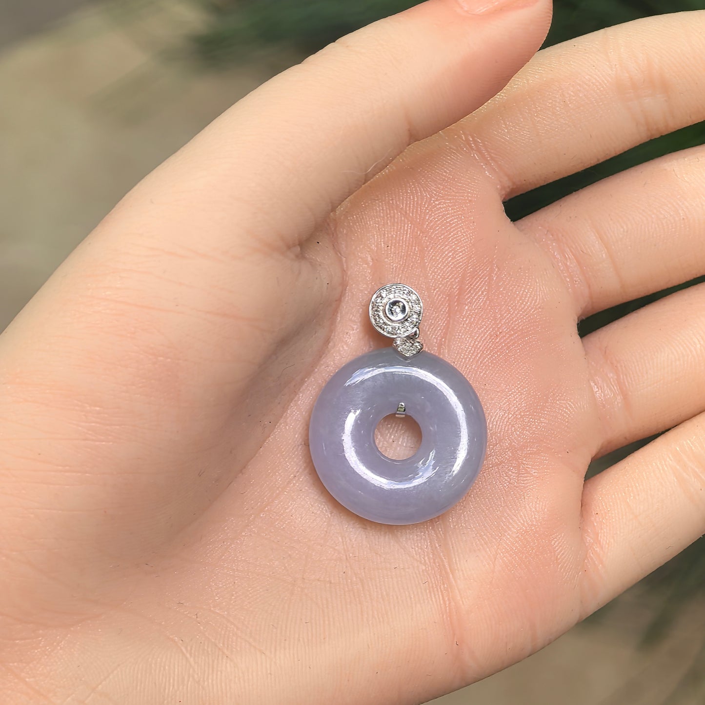 Lavender jadeite donut pendant resting in an open palm, showing its purple color and 18K gold setting with diamond accents.