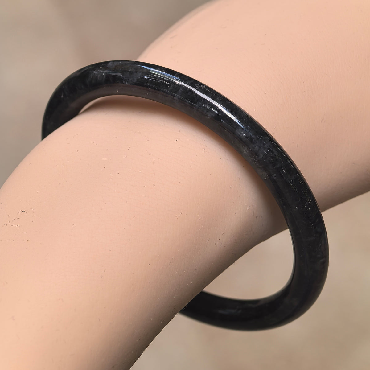 Angled wrist view of a slim black and gray jadeite bangle with a polished round-bar profile.
