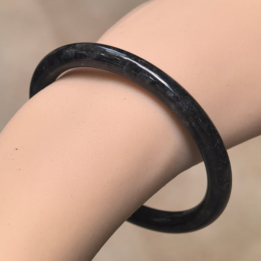 Angled wrist view of a slim black and gray jadeite bangle with a polished round-bar profile.